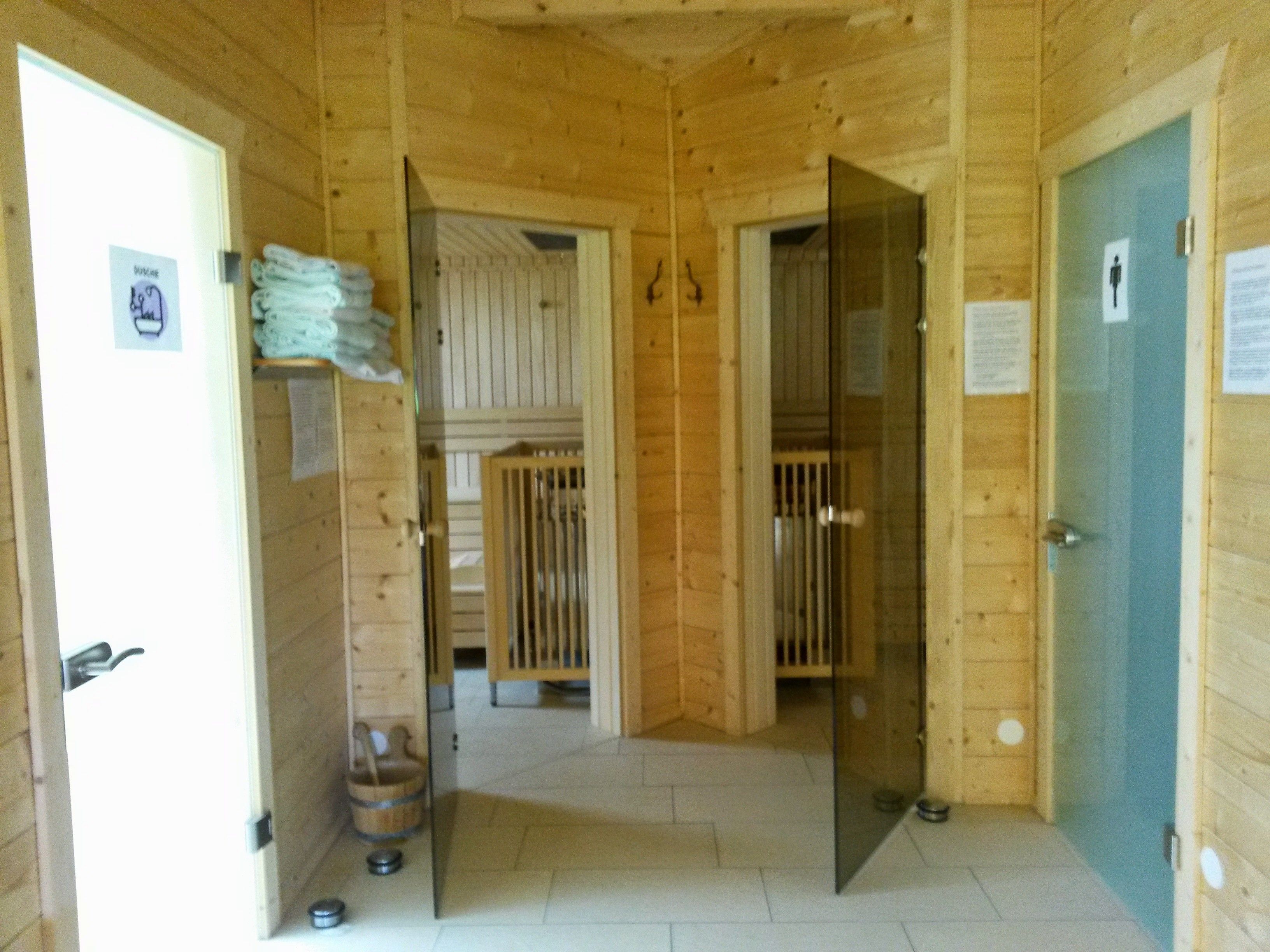 Pohled do interiéru sauny s dřevěnými stěnami, skleněnými dveřmi a ručníky.