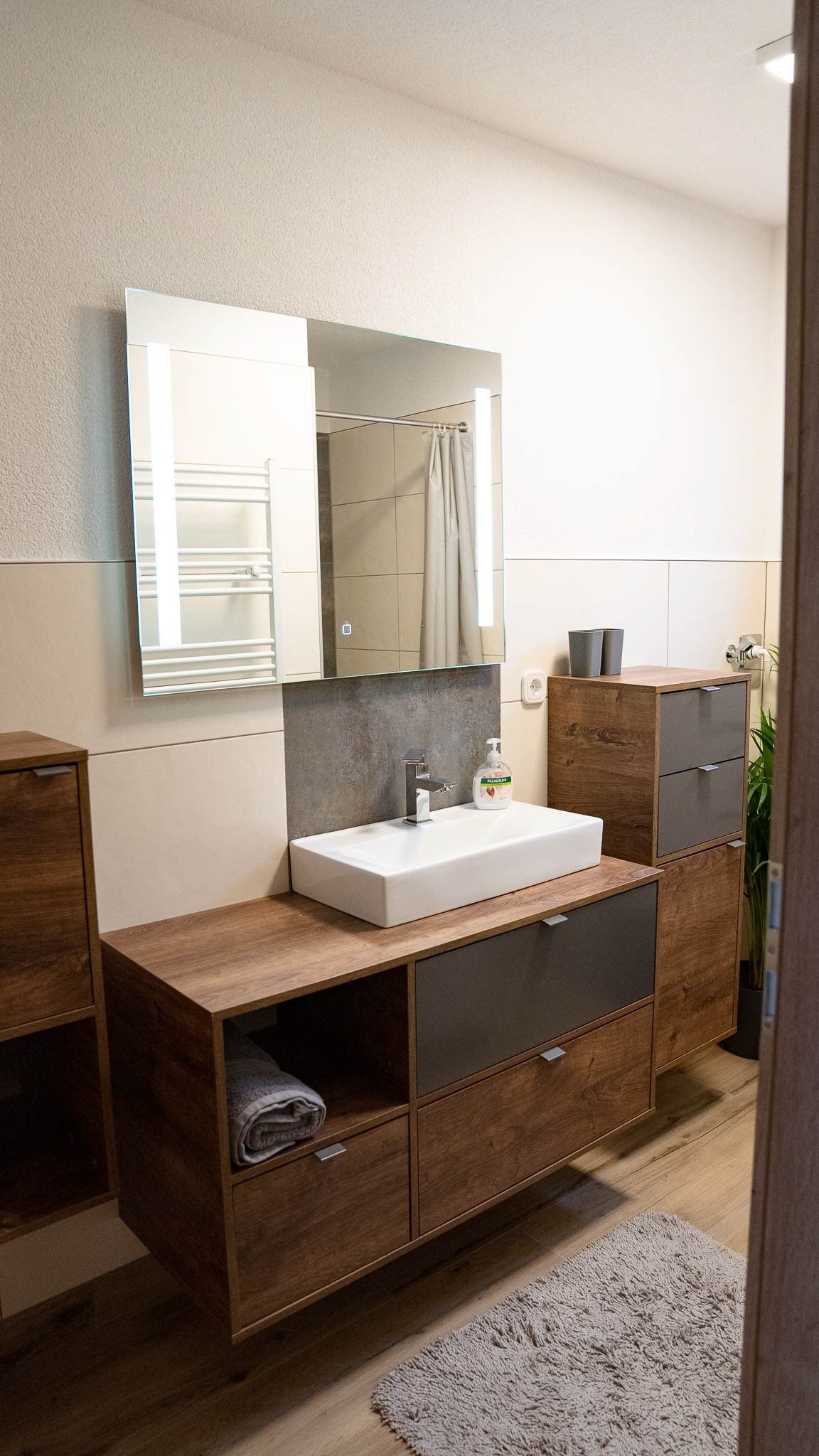 Moderní koupelna s dřevěnými skříňkami, umyvadlem a zrcadlem.