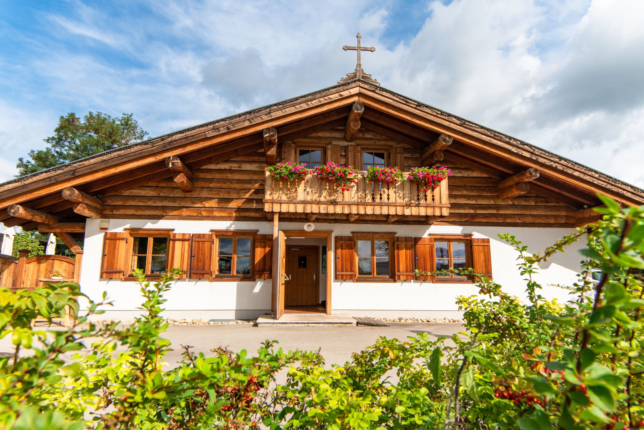 Tradiční dřevěný dům s balkonem a květinovými truhlíky, v pozadí modrá obloha.
