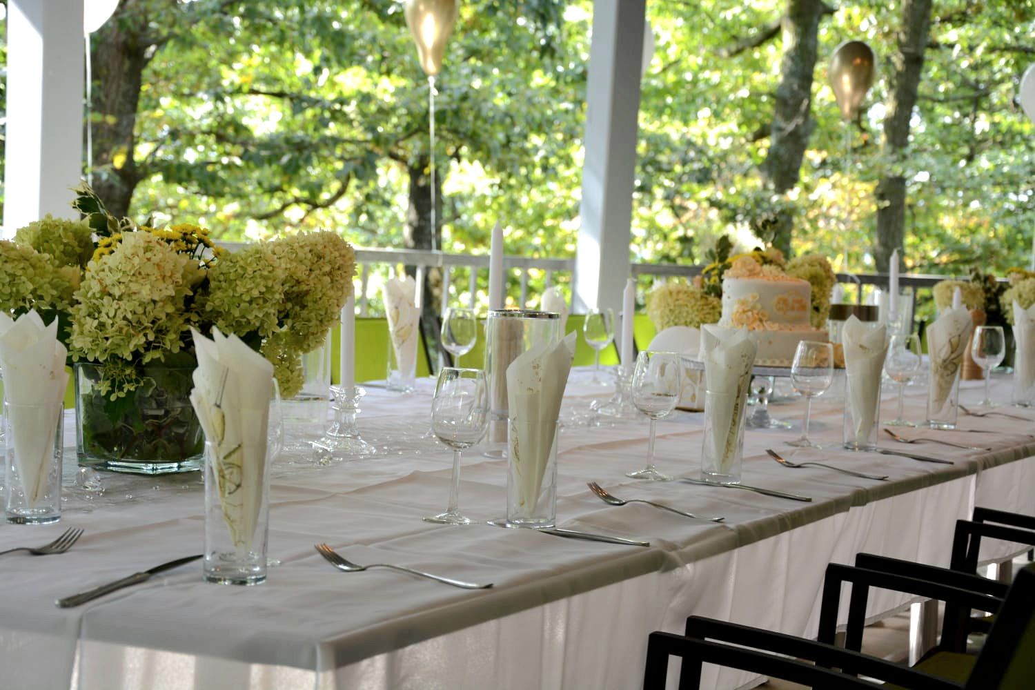 Slavnostně prostřený stůl v bílém na terase s květinami a svíčkami.