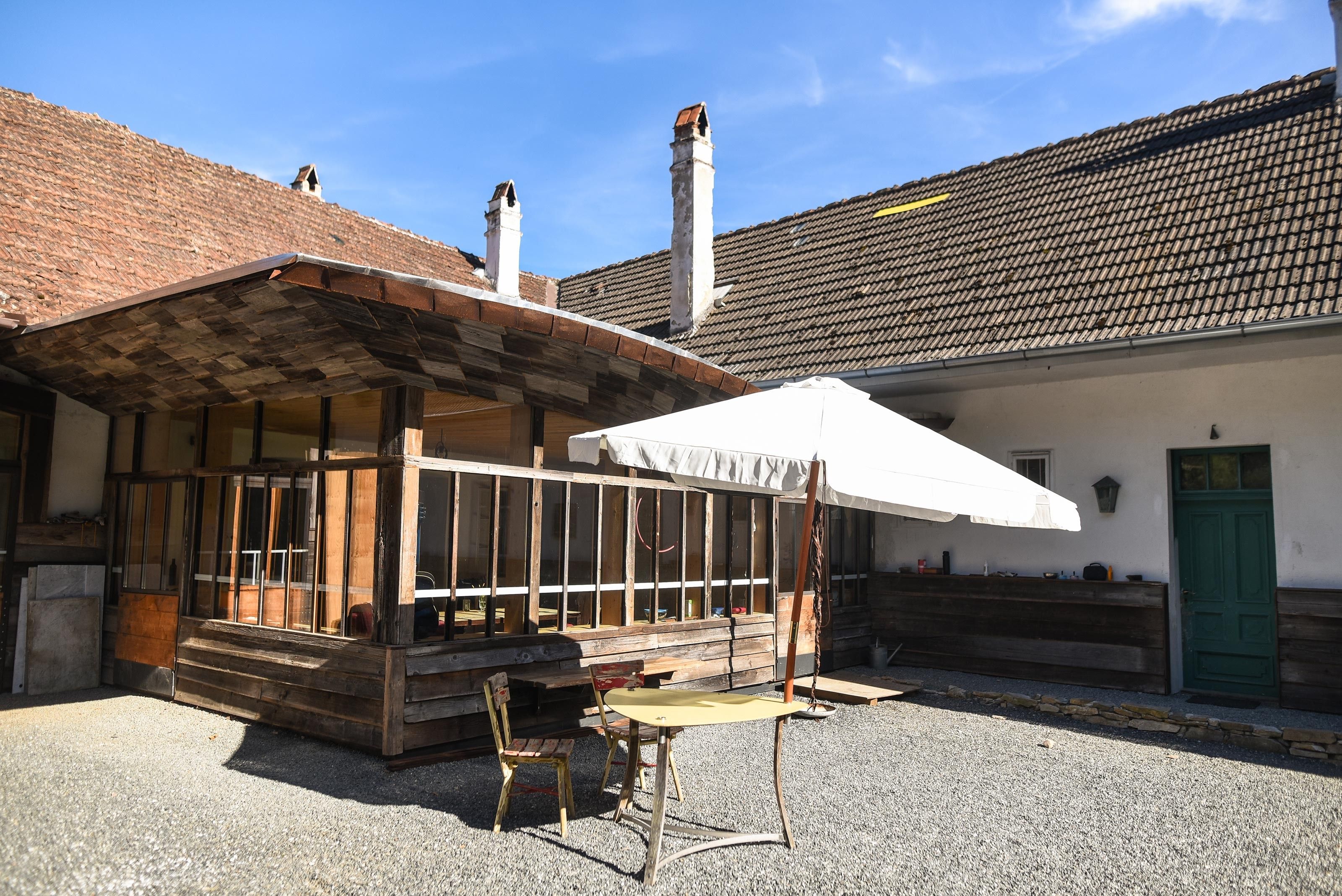 Rustikální vnitřní dvůr s dřevěnou přístavbou, stolem a židlemi pod slunečníkem.