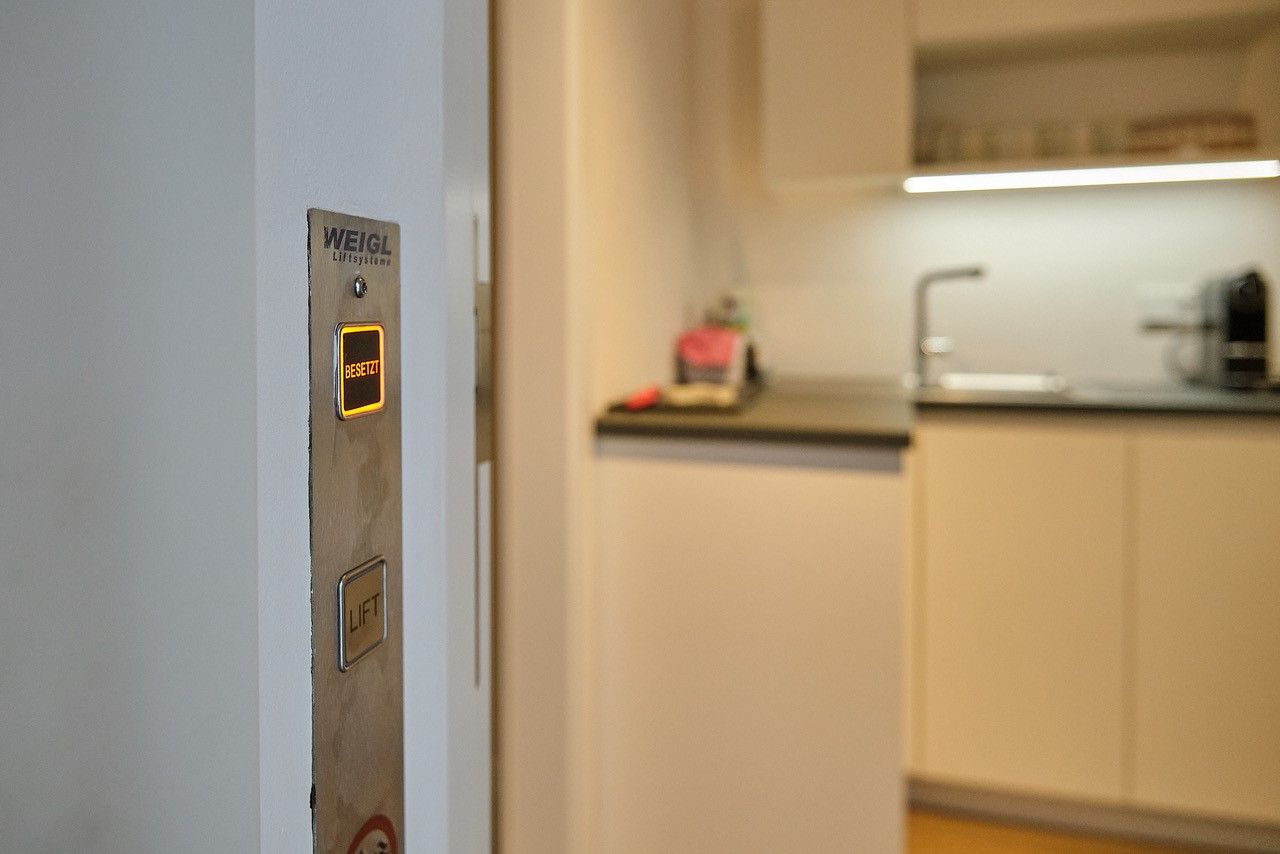 V moderním obývacím pokoji vedle kuchyně se rozsvítí výtahové tlačítko s nápisem "Busy".
