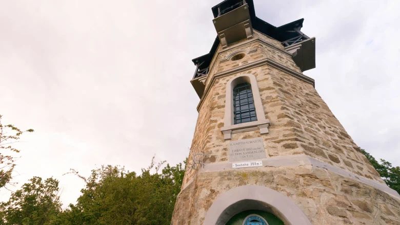 Kamenná rozhledna s okny a nápisem, obklopená stromy.