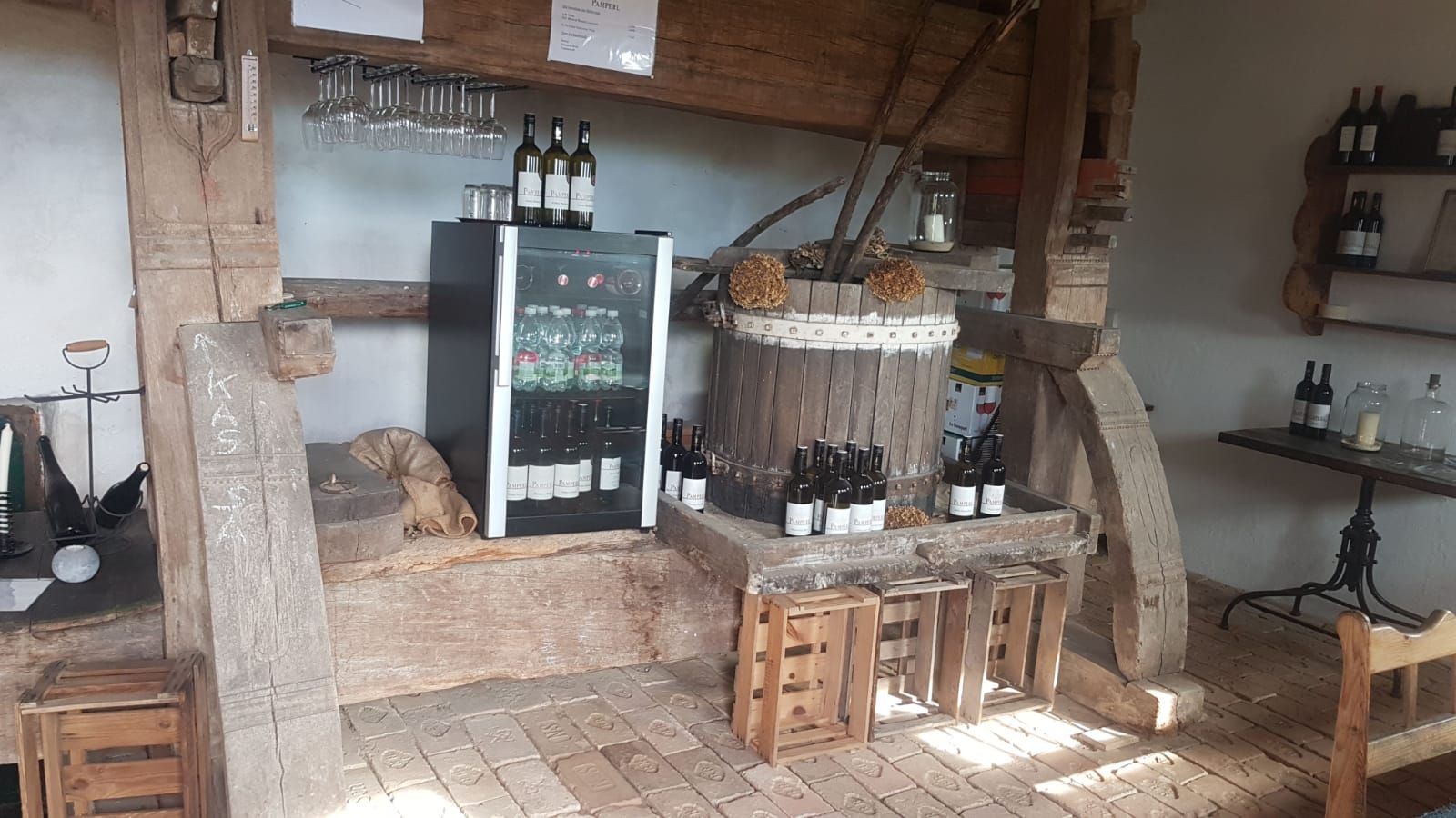 Pohled do interiéru rustikální vinárny s lahvemi vína, sklenicemi a lednicí.