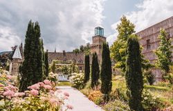 Blühender Schlossgarten von Schloss Rothschild in Waidhofen an der Ybbs mit Blumenbeeten, schlanken Zypressen und dem gläsernen Turm des historischen Gebäudes