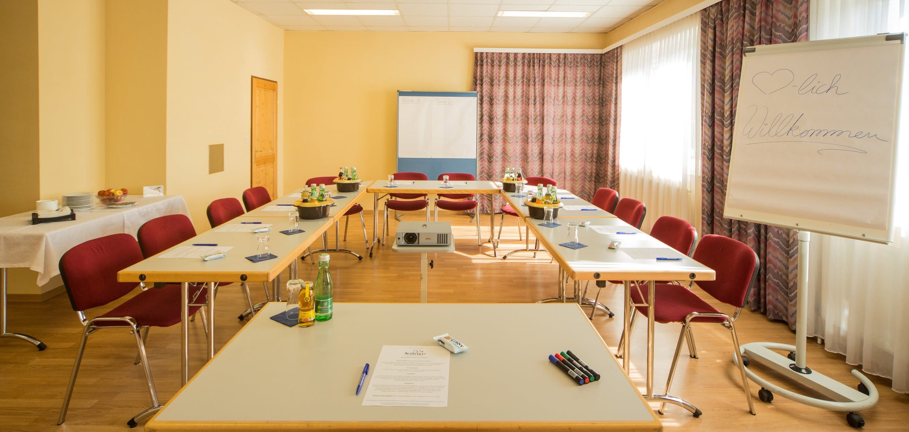 Seminární místnost s uspořádáním stolů do tvaru písmene U, flipchartem a nápoji.