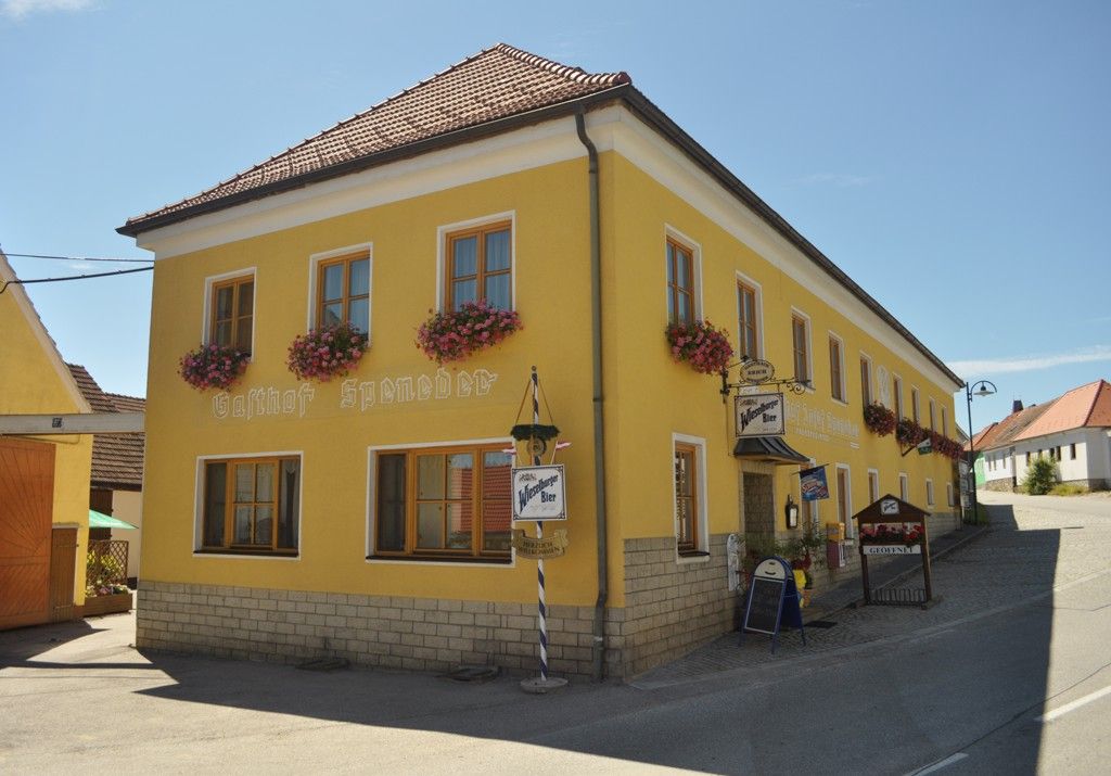 Žlutá budova s nápisem "Gasthof Speneder", zdobená květinami.