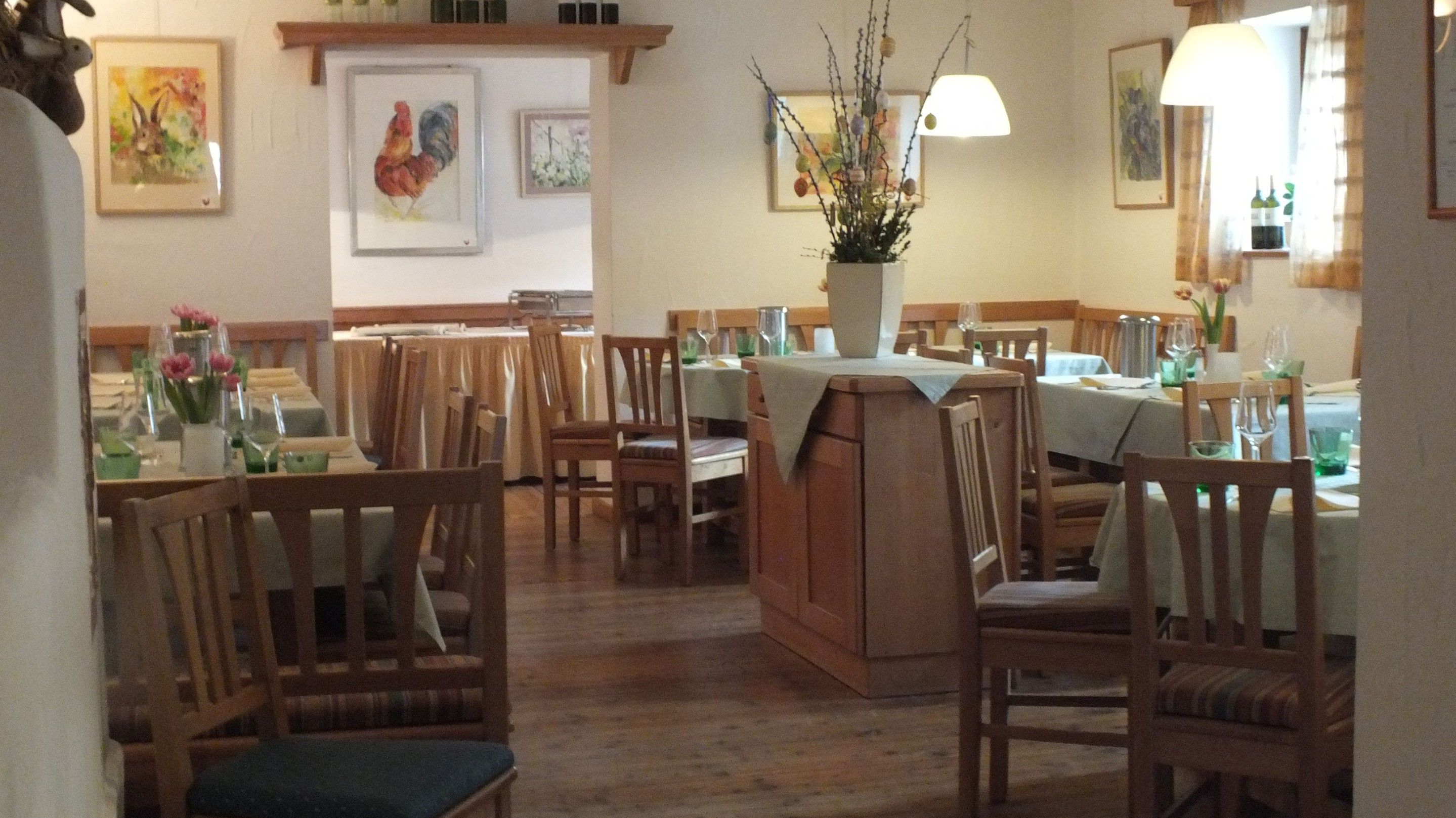 Útulná restaurace s dřevěným nábytkem, prostřenými stoly a vázami s květinami. Obrazy zvířat na stěnách.