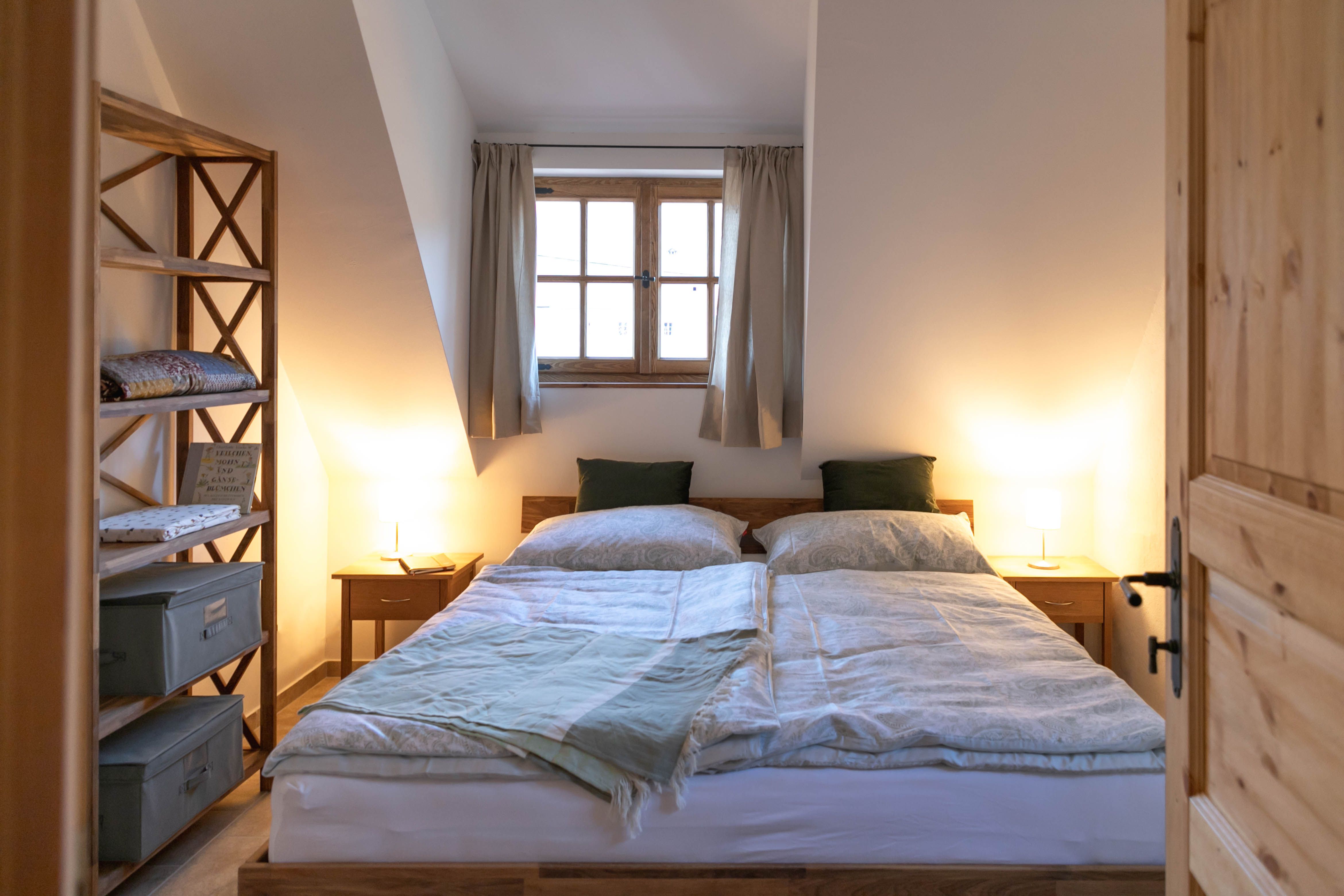 Útulná ložnice s manželskou postelí, dřevěným nábytkem a oknem se závěsy.