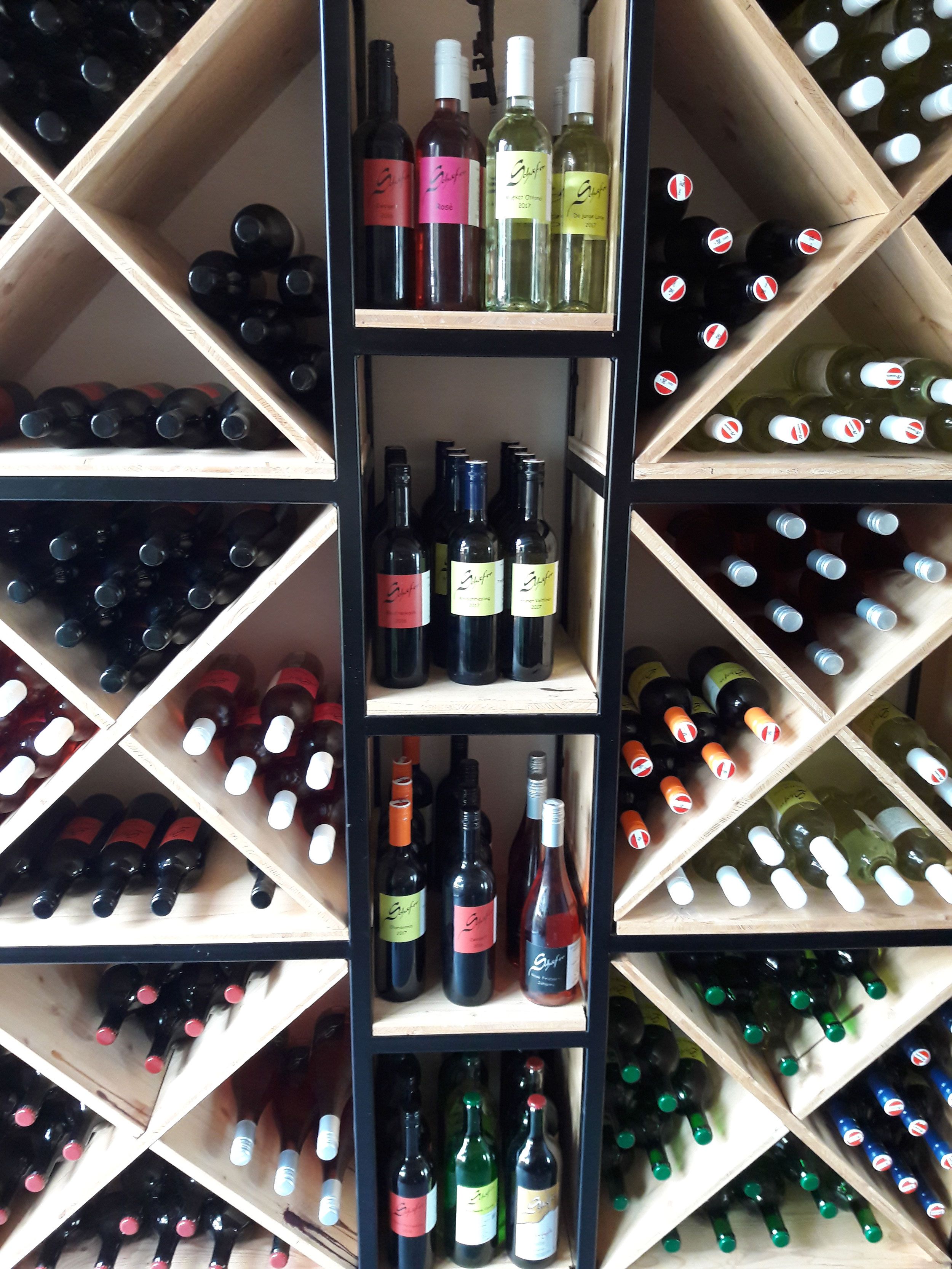 Lahve na víno na dřevěné polici s diagonálními policemi.