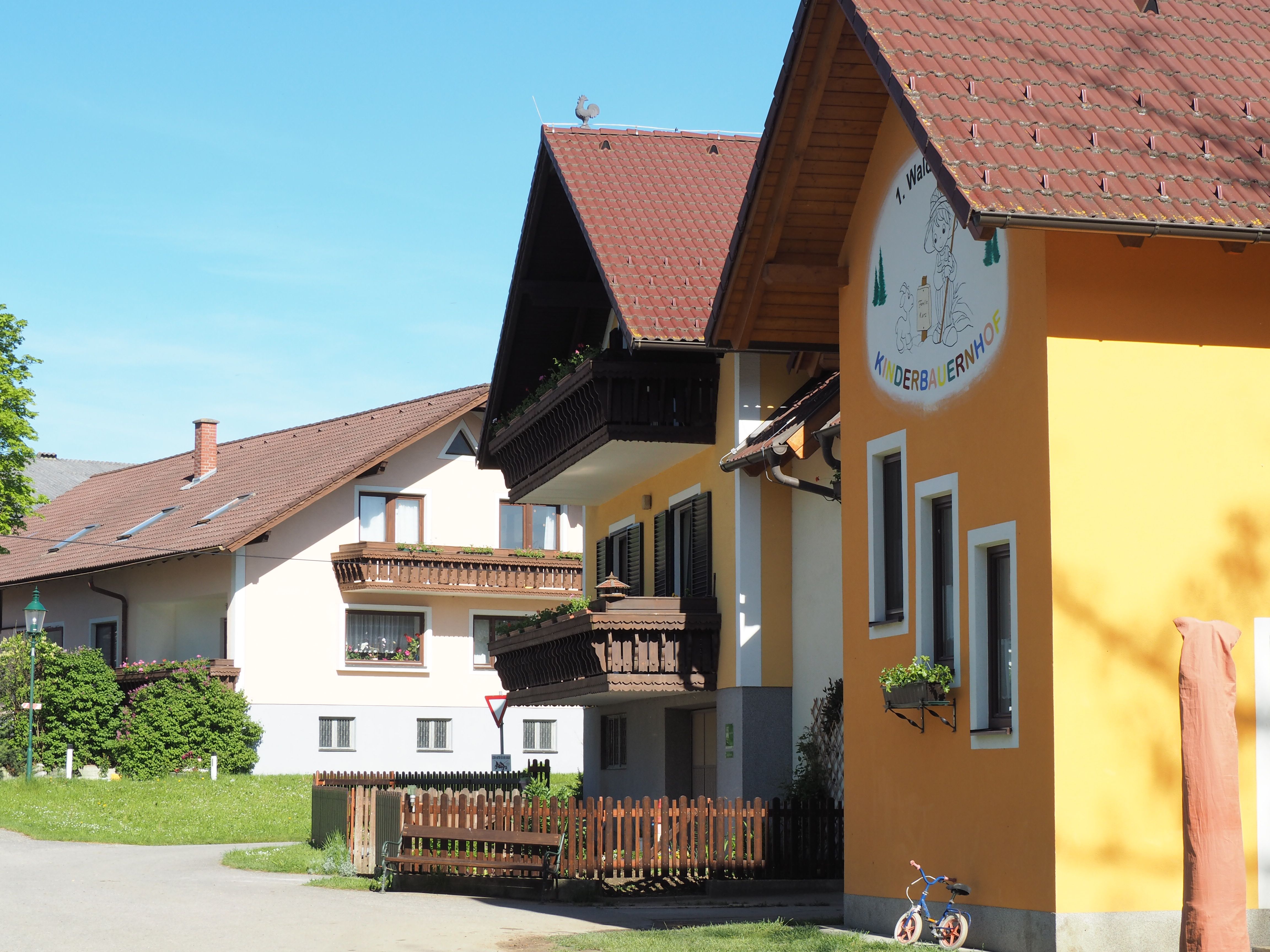 Budova dětského statku Waldviertel se žlutou fasádou a dřevěnými balkony, obklopená zelenou krajinou.