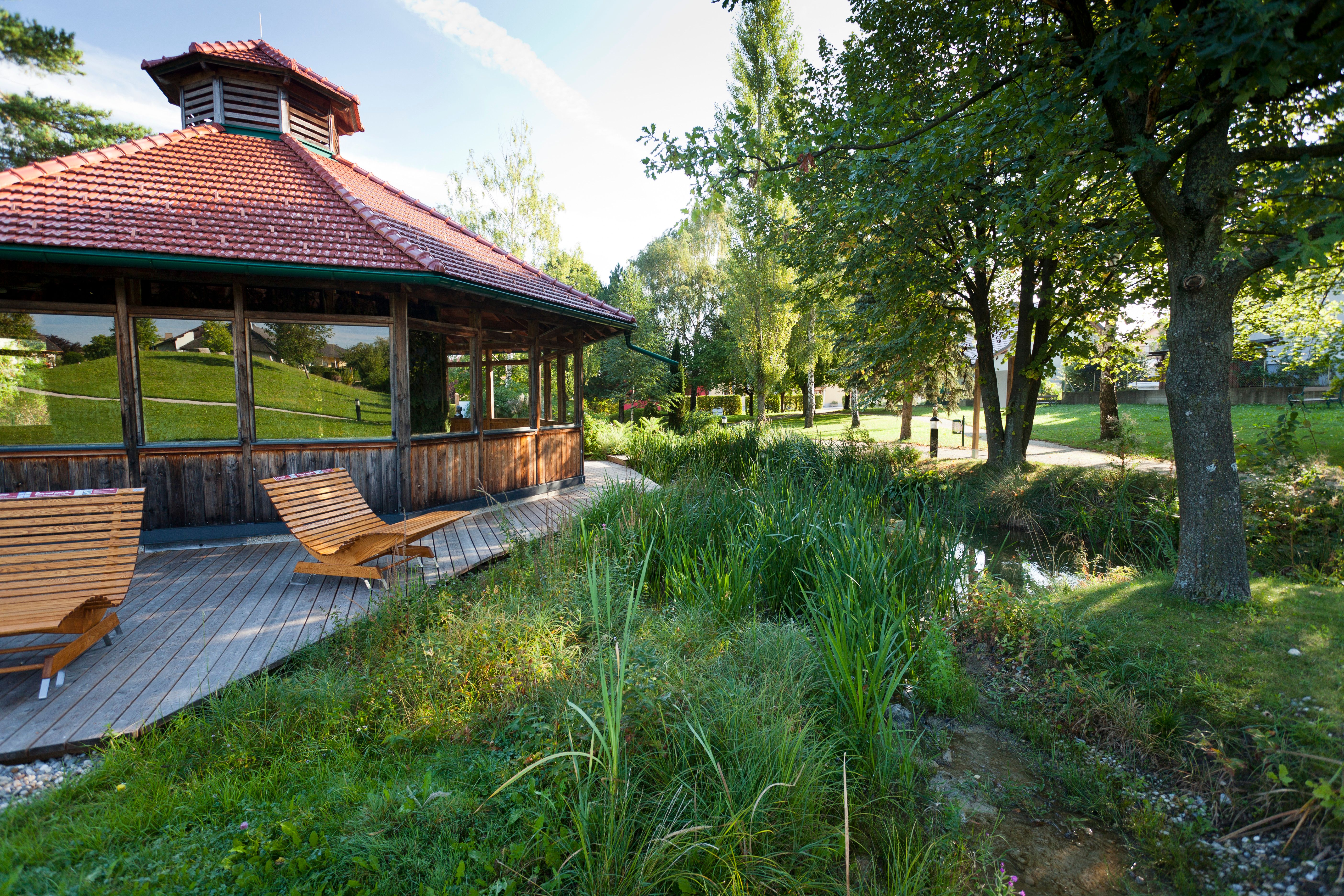 Dřevěný pavilon s lehátky v zeleném parku.