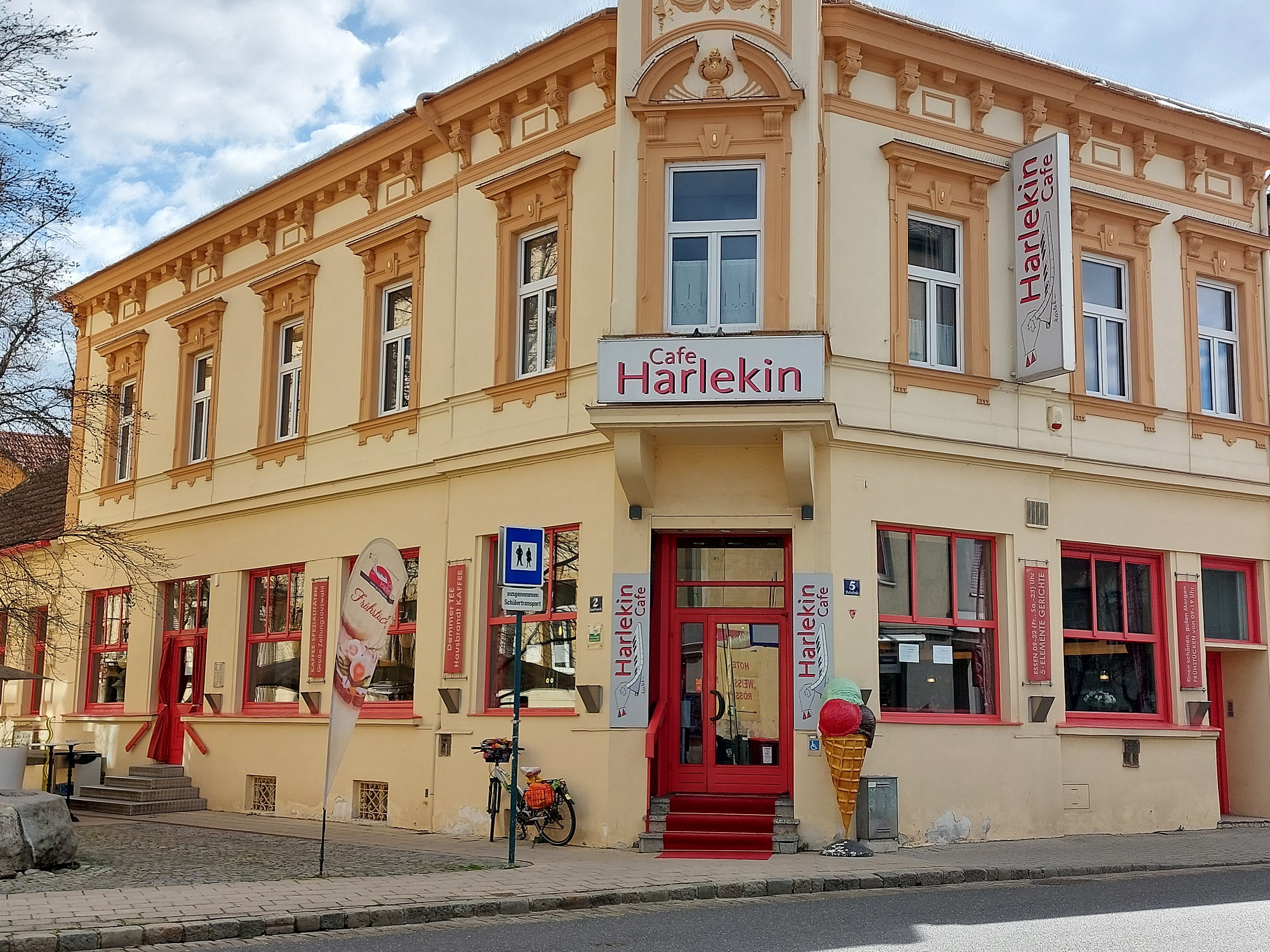 Pohled zvenčí na kavárnu Restaurant Harlekin se žlutou fasádou a červenými okny.