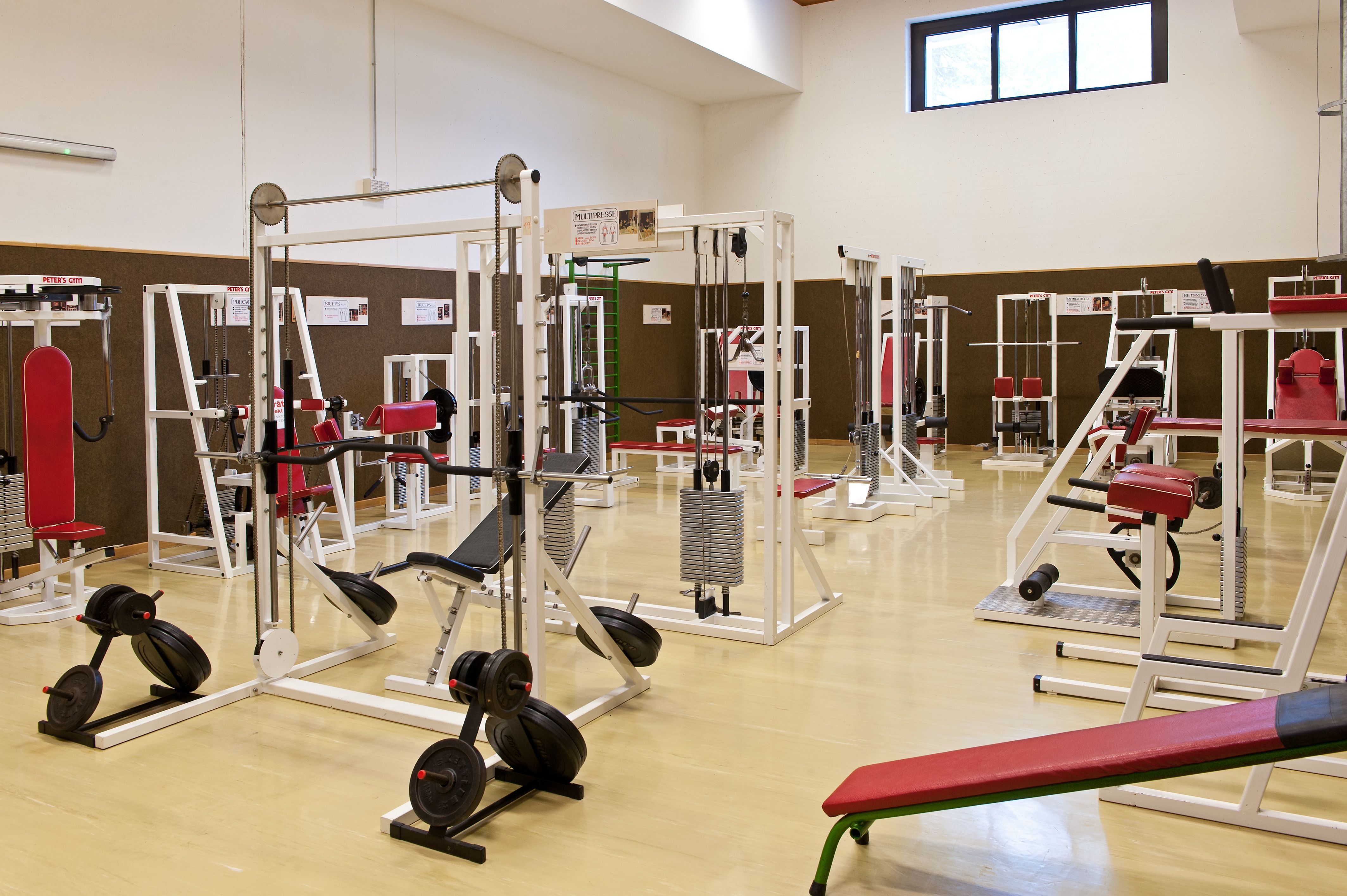 Fitness studio s různými cvičebními stroji a červenými polštáři.