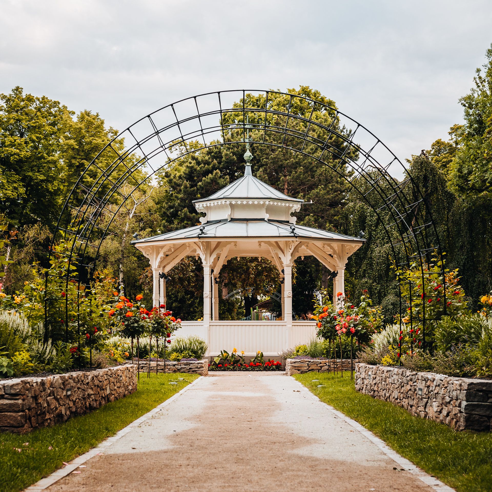 Zelený městský park s romantickým altánem, růžovou zahradou a klenutým obloukem