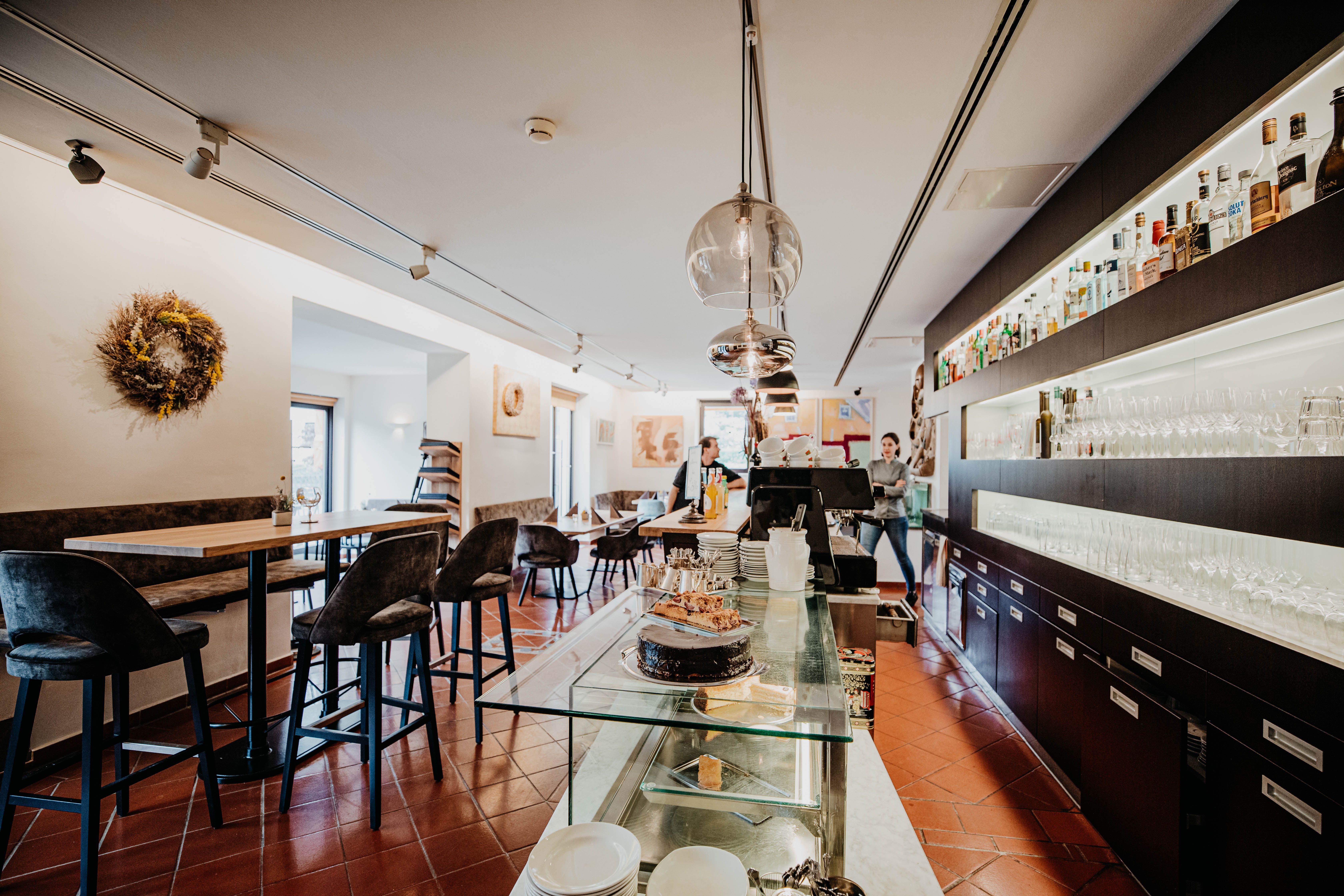 Pohled do interiéru moderní restaurace s barem, stoly a židlemi.