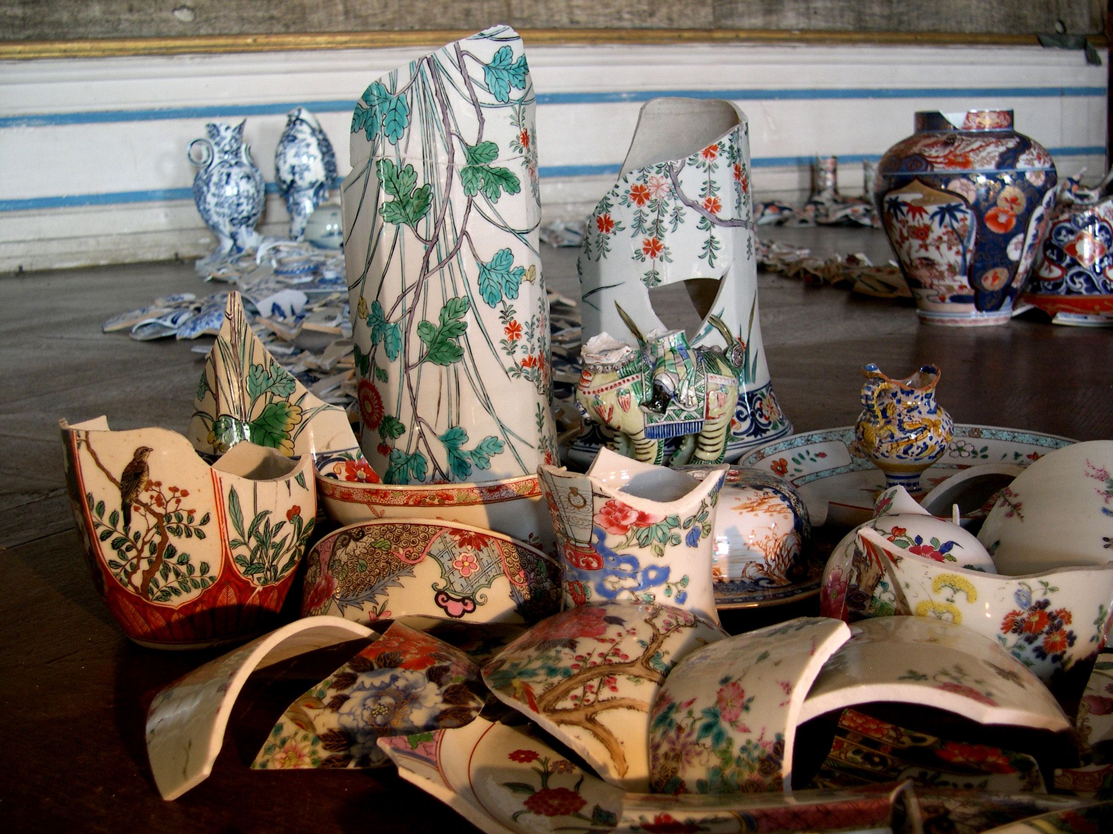 Rozbité kousky porcelánu s barevnými vzory rozmístěné na podlaze.