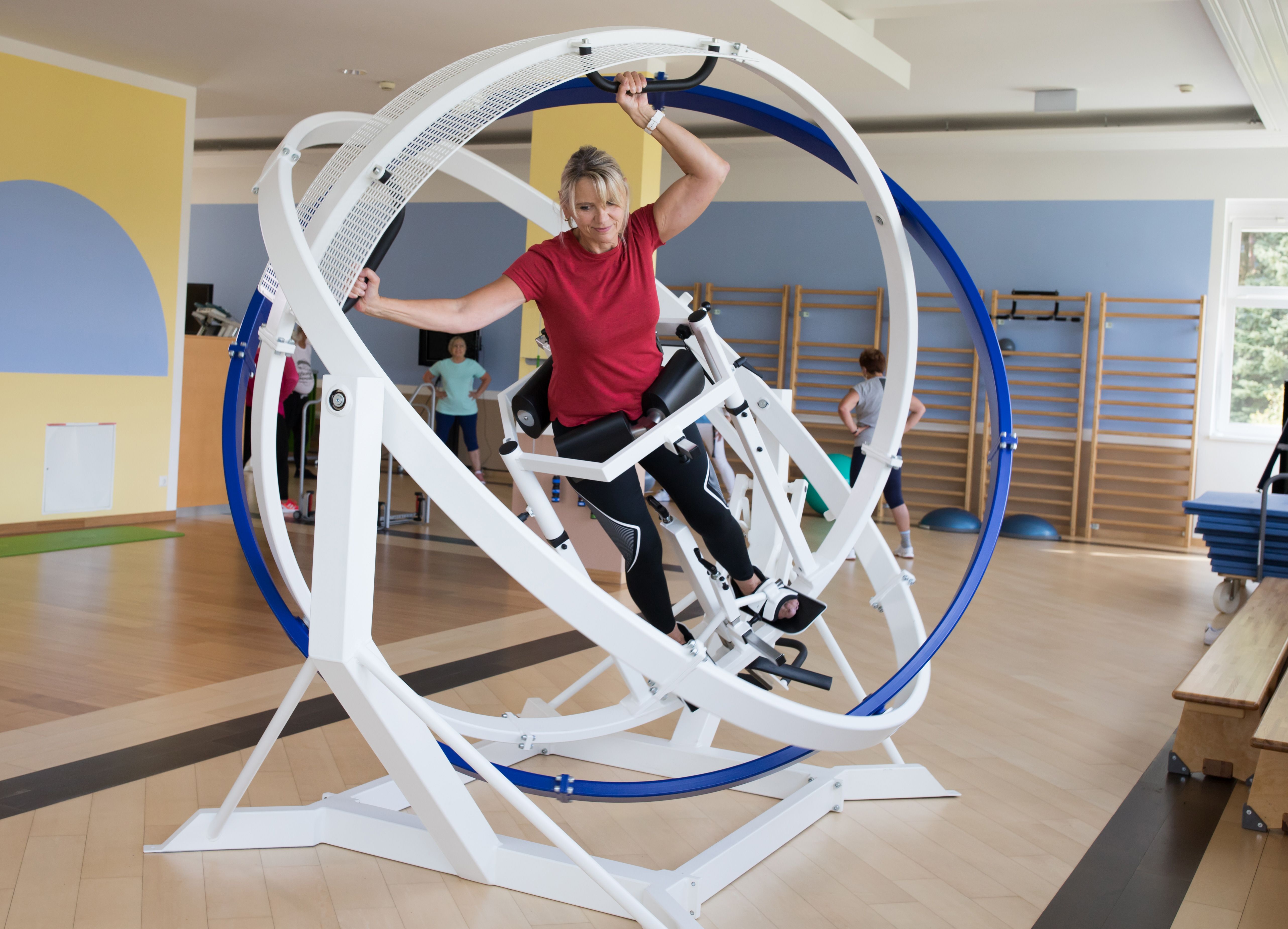 Žena cvičí na posilovacím stroji s rotujícími kruhy ve fitness centru.