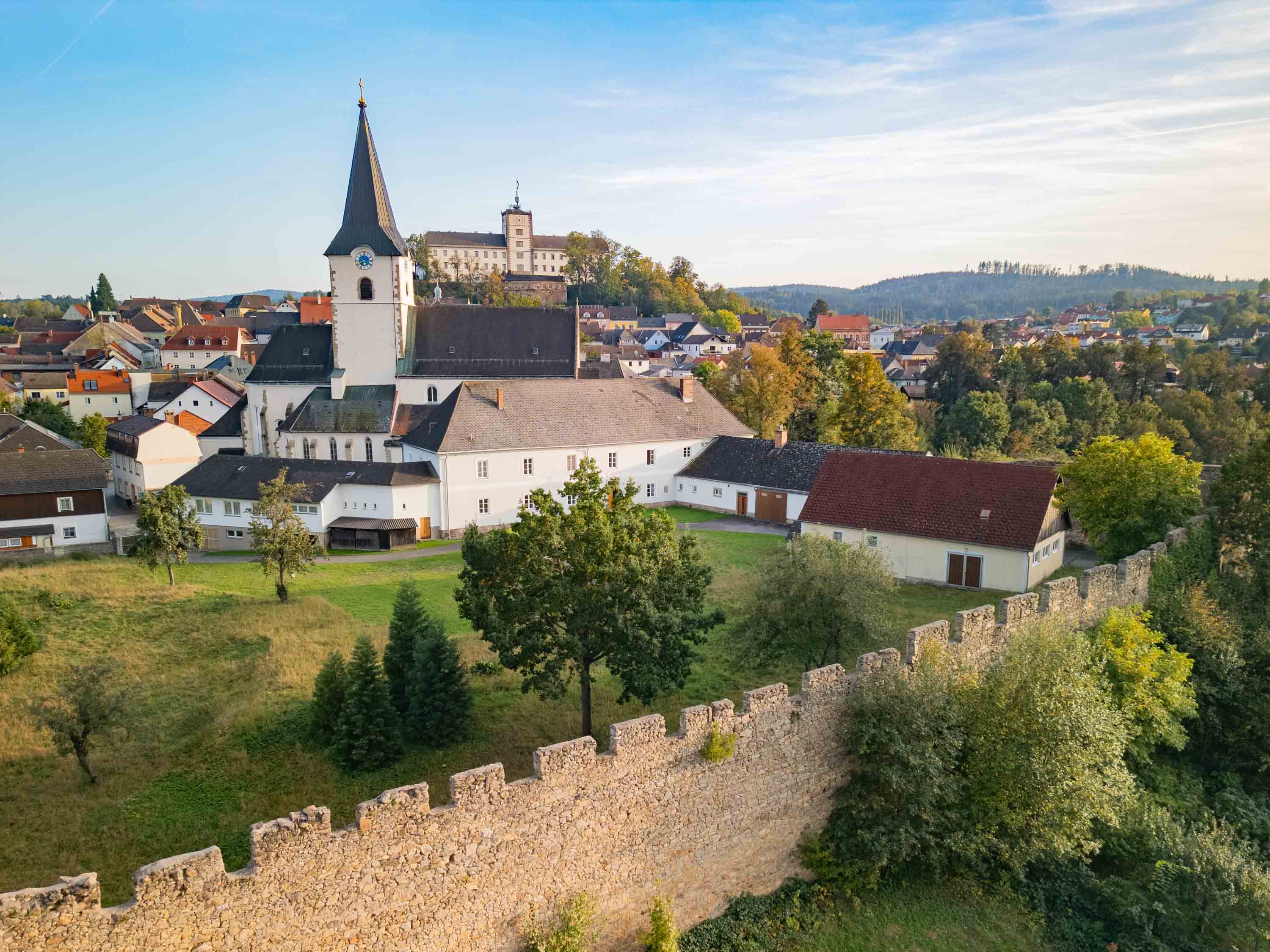 Letecký pohled na město s kostelem a městskými hradbami v popředí.