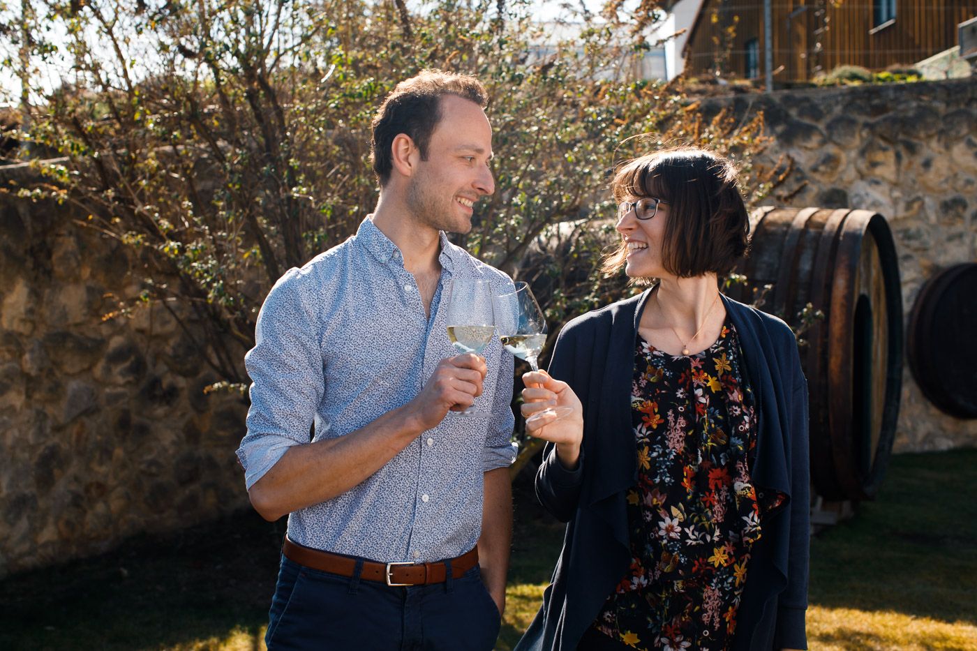 Muž a žena si venku cinknou skleničkami vína.