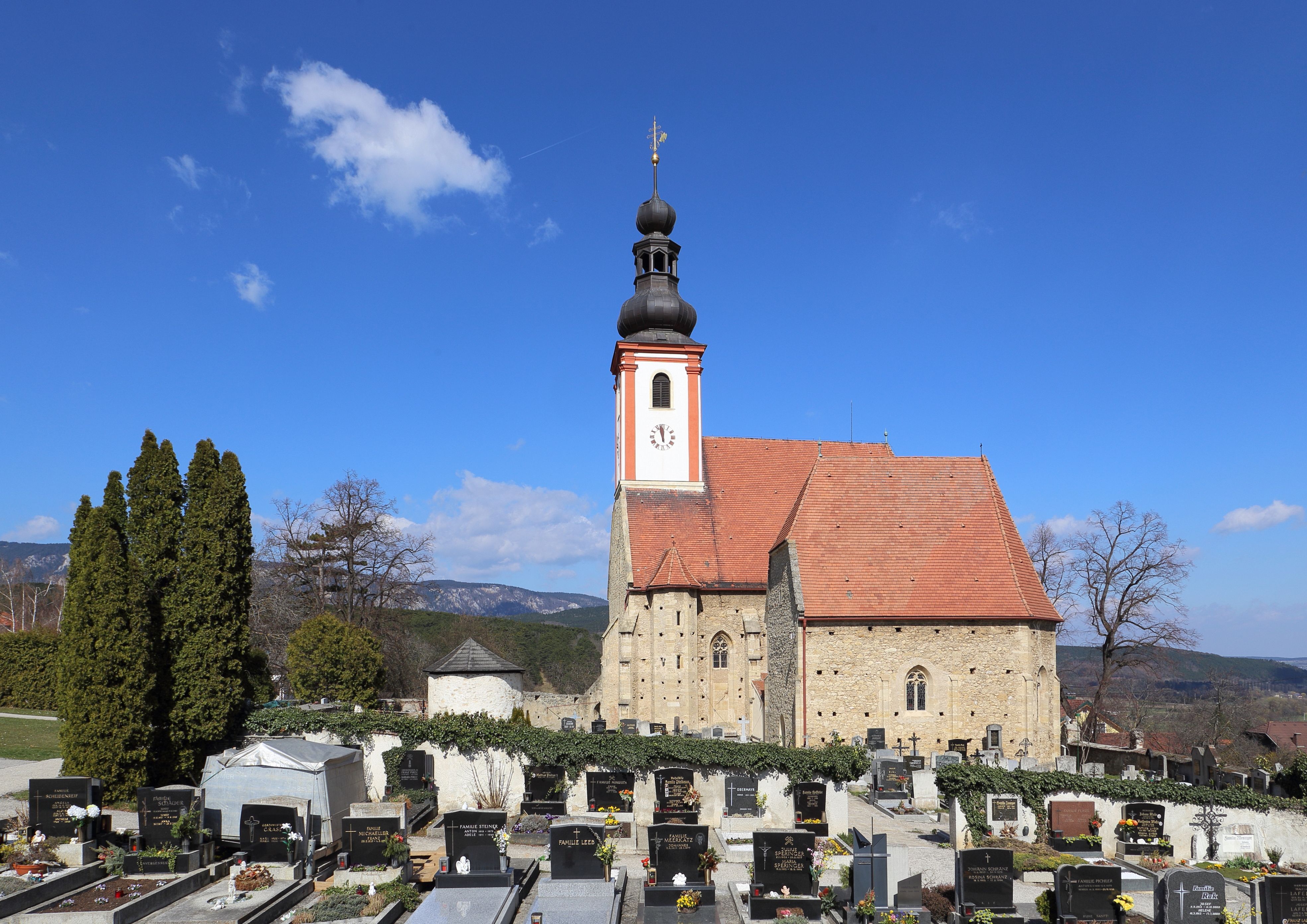 Kostel se hřbitovem v popředí a modrou oblohou.