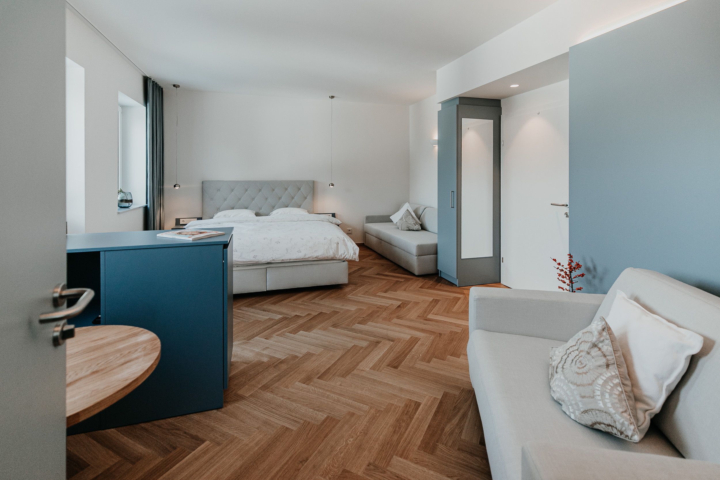 Moderně zařízený hotelový pokoj s manželskou postelí, pohovkou a dřevěnou podlahou.