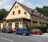 Žlutý hostinec s červenými květy a zaparkovanými auty před ním.