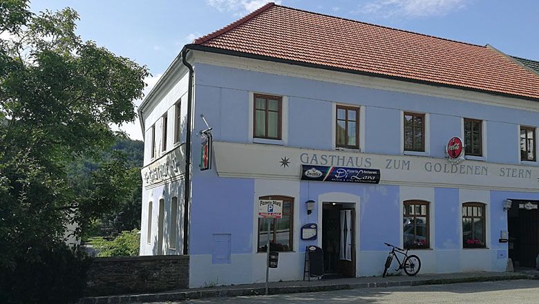 Dvoupatrová budova s nápisem "Gasthaus zum Goldenen Stern" a s jízdním kolem před ní.