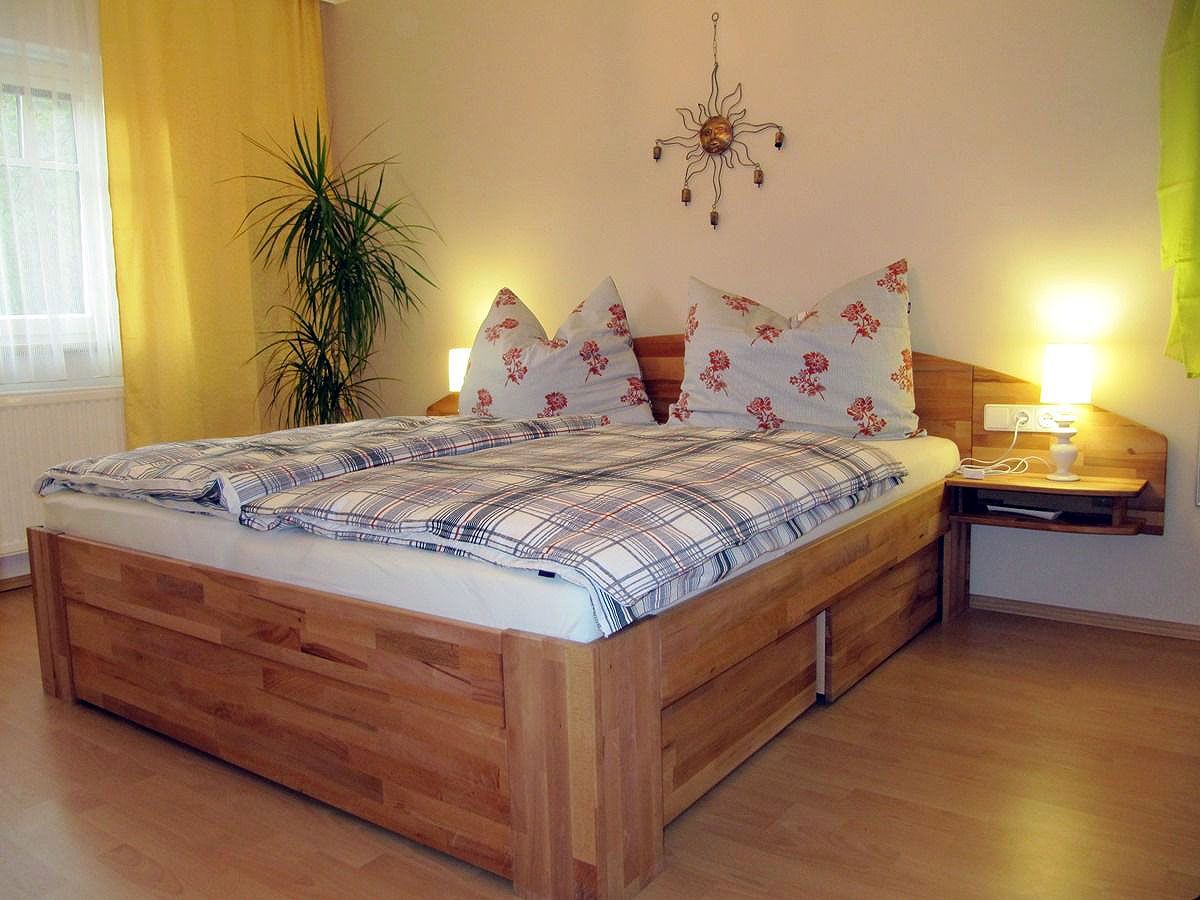 Útulná ložnice s manželskou postelí, rostlinami a nástěnnou dekorací.