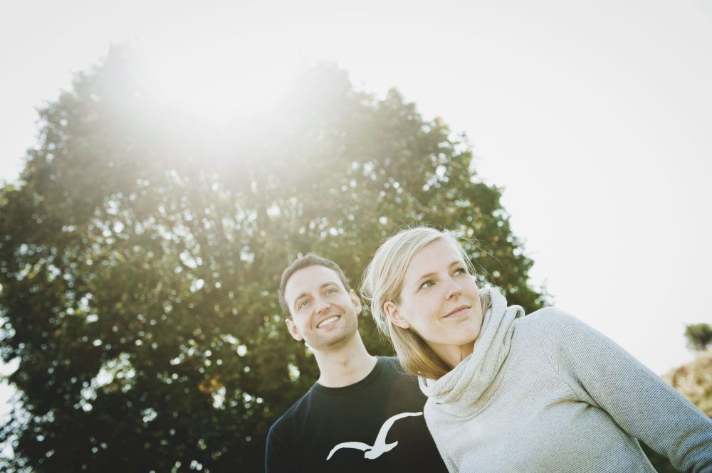 Muž a žena stojí venku před stromem a skrz listy prosvítá slunce.