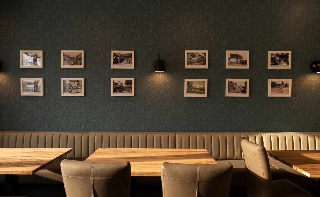 Pohled do interiéru restaurace s čalouněnými lavicemi a dřevěnými stoly, zdobené zarámovanými fotografiemi na stěně.