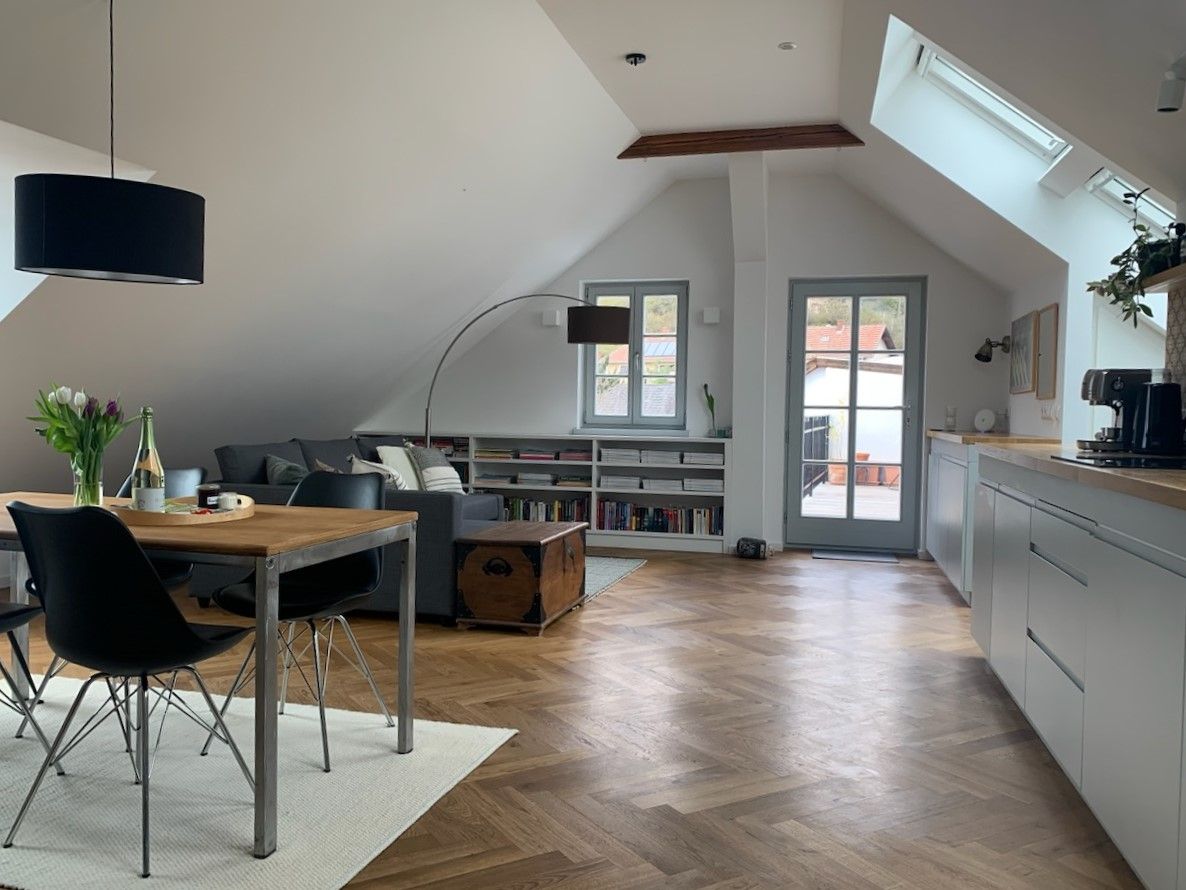 Moderní podkrovní byt s dřevěnou podlahou, jídelním stolem, pohovkou a přístupem na balkon.