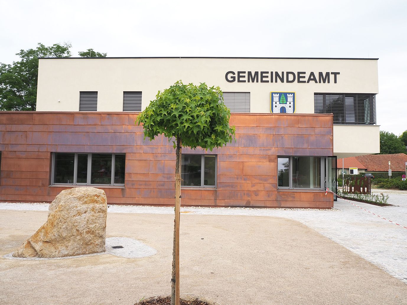 Moderní budova obecního úřadu v Sieghartskirchenu se stromem a kamenem v popředí.