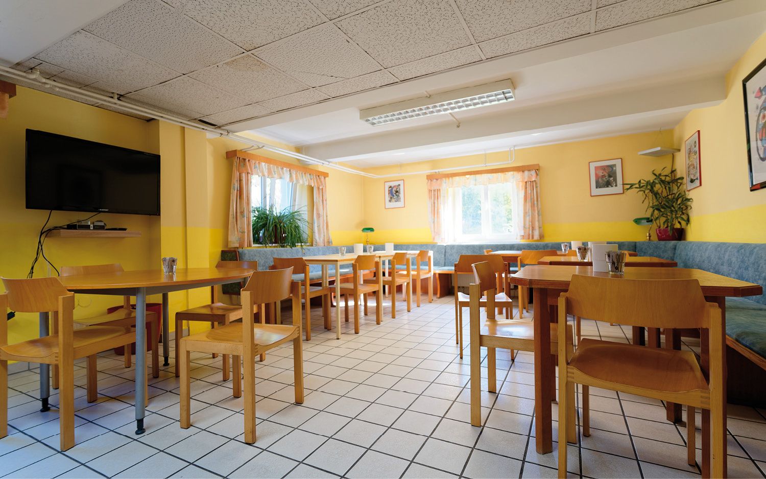 Světlá snídaňová místnost s dřevěným nábytkem, žlutými stěnami a velkými okny.