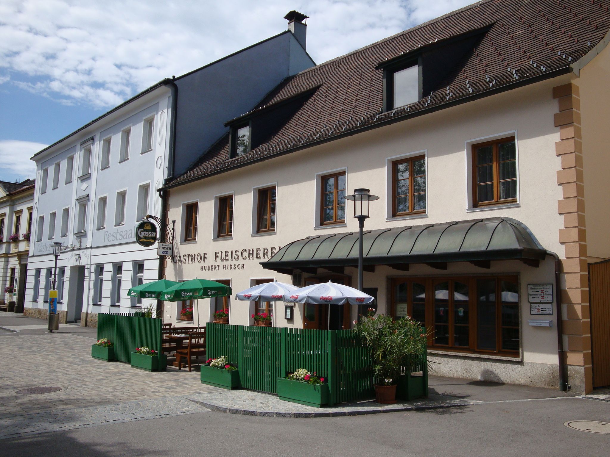 Restaurace řeznictví Hirsch s venkovní terasou a slunečníky.