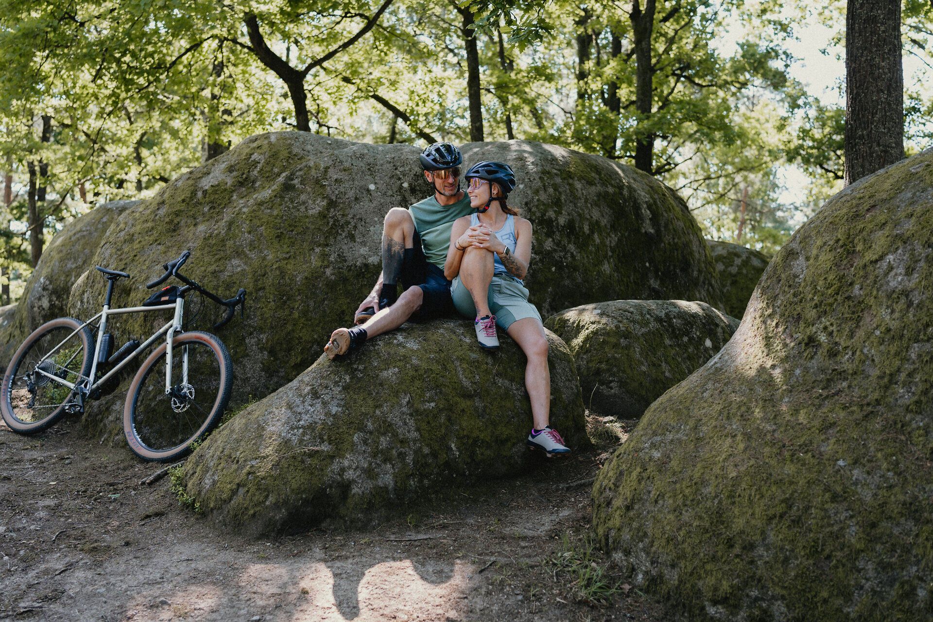 Muž a žena v cyklistickém oblečení sedí na kameni a povídají si, jejich kola jsou opřená o další kámen vedle nich.