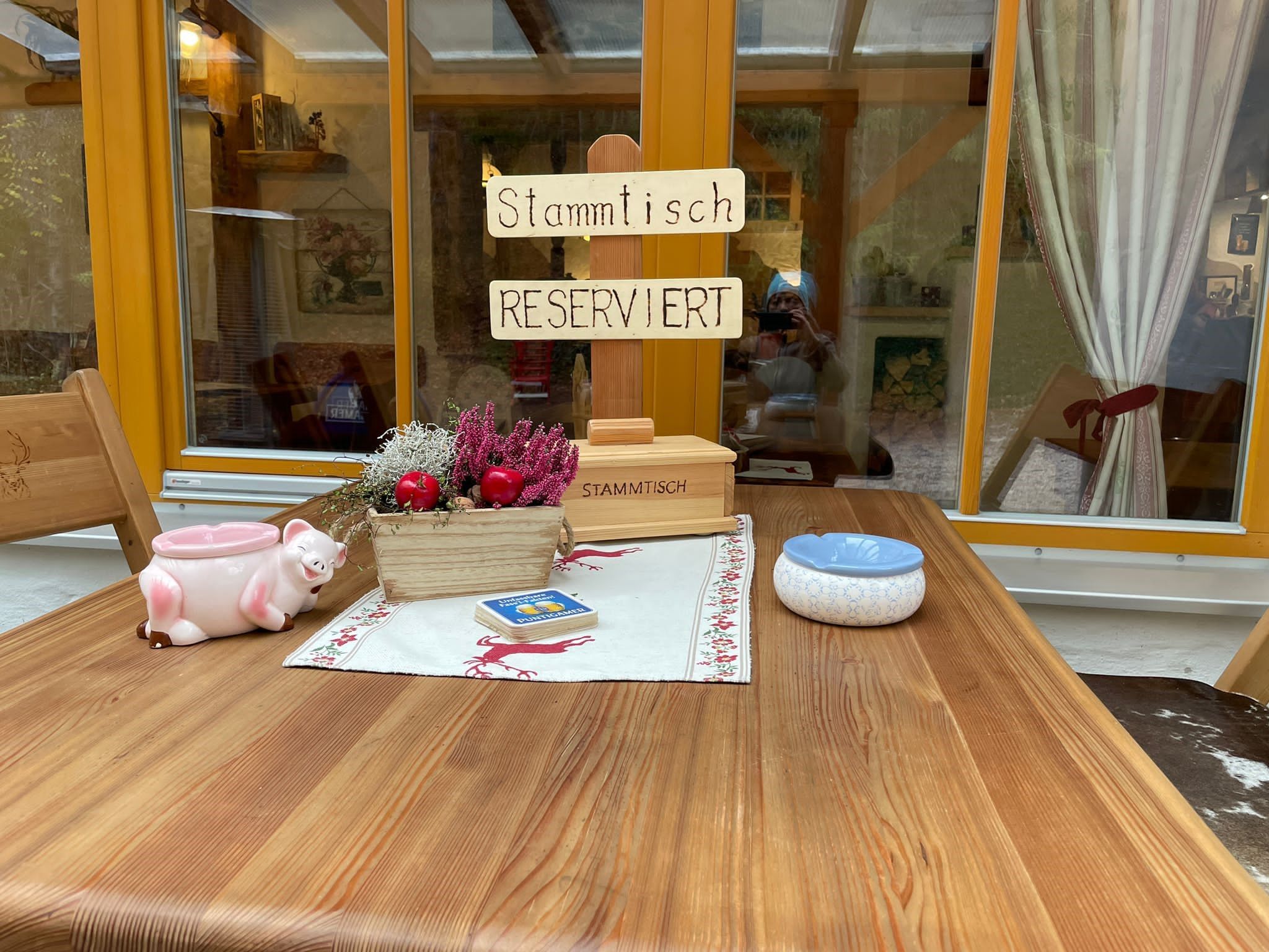 Rustikální stůl s nápisem "Stammtisch Reserviert", dekoracemi a popelníkem.