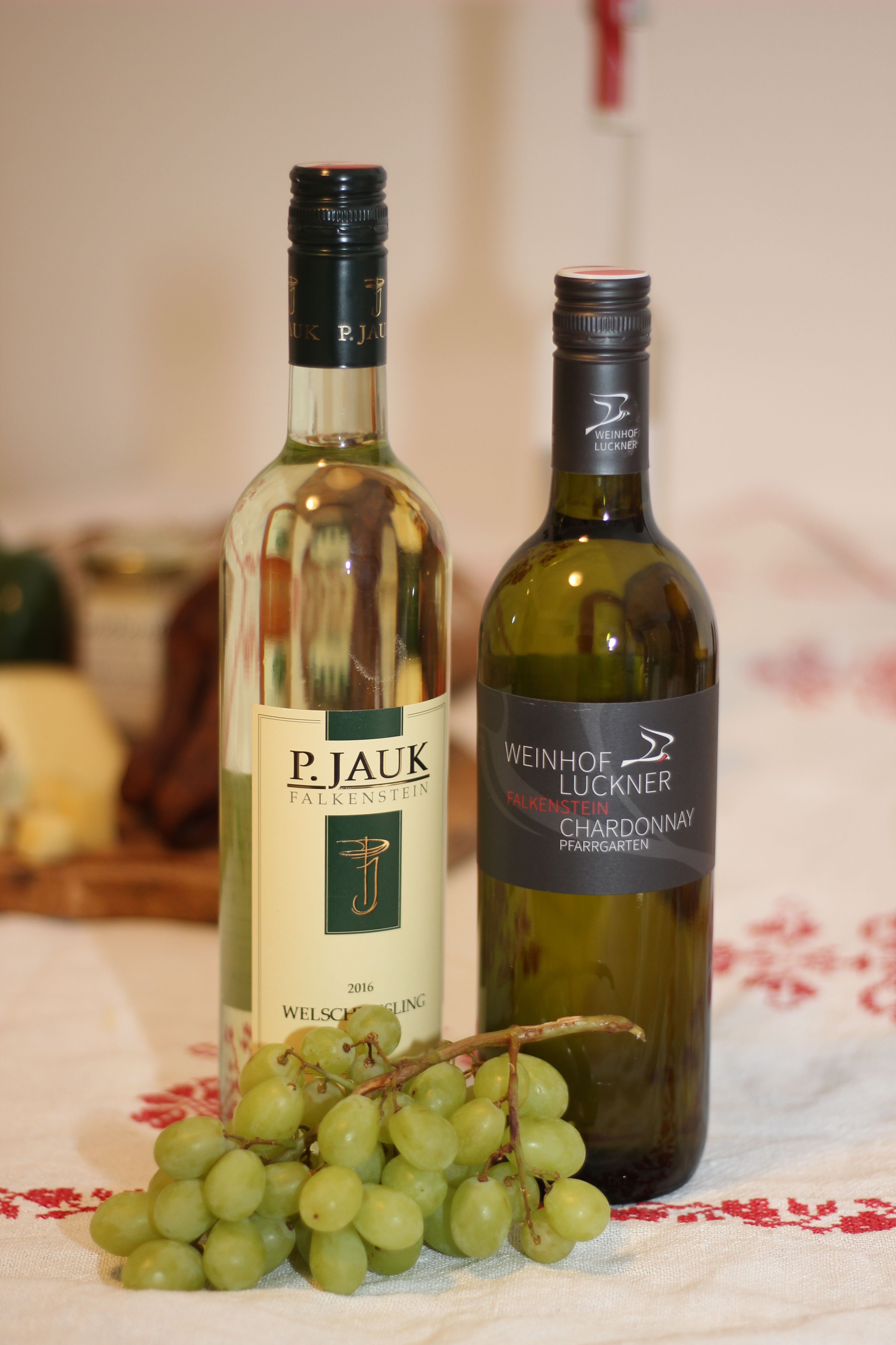 Dvě láhve vína a trs zelených hroznů na stole.