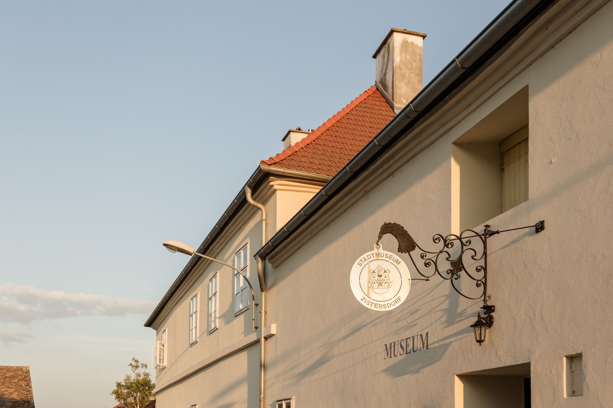 Pohled zvenčí na městské muzeum v Zistersdorfu s ozdobným nápisem a sloupem veřejného osvětlení v popředí.