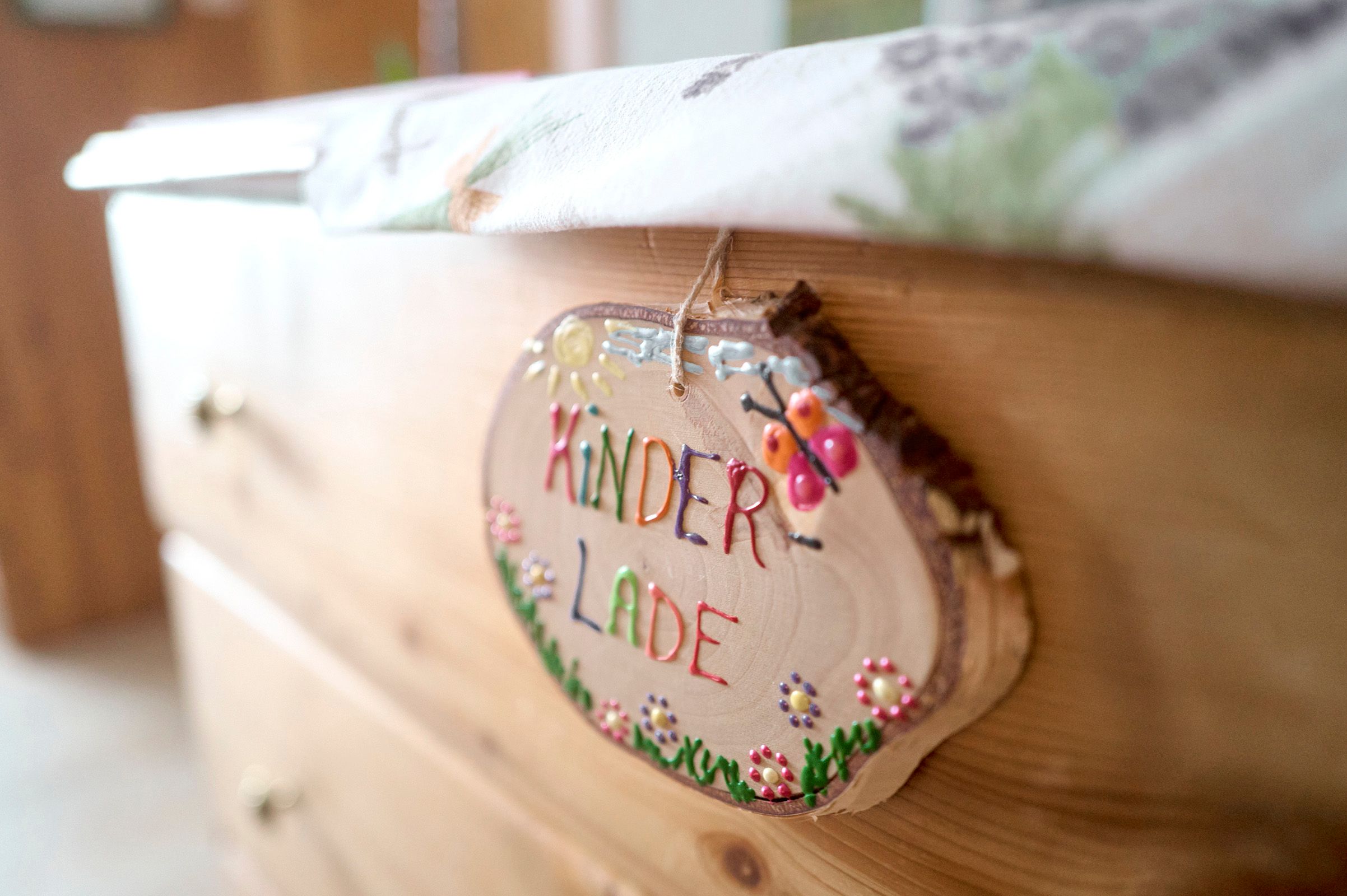 Detailní záběr dřevěné cedule s nápisem "Kinderlade" na komodě.