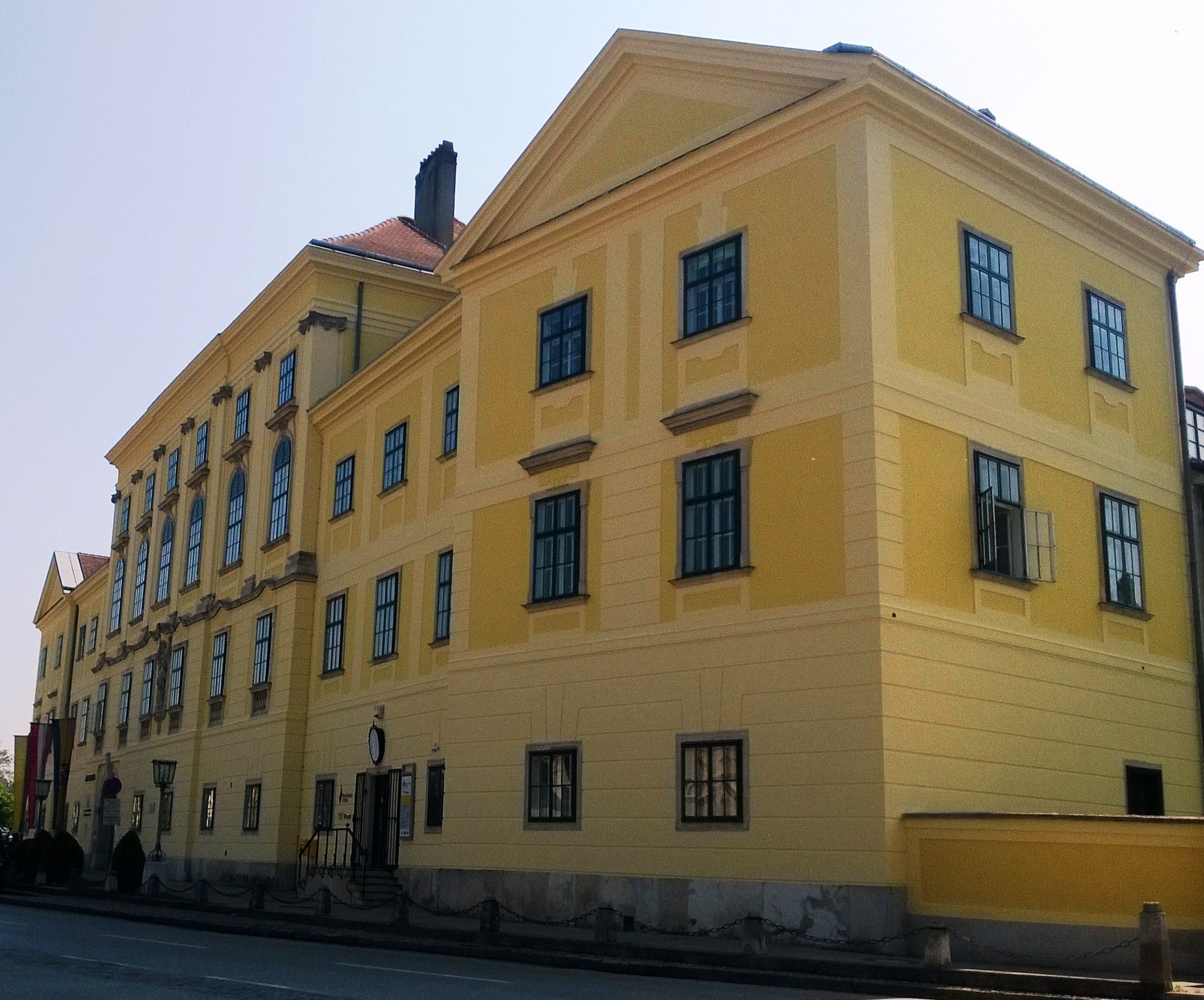 Žlutá historická budova s mnoha okny a sedlovou střechou.