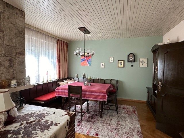 Útulný obývací pokoj s jídelním stolem, rohovou lavicí, kobercem a nástěnnými hodinami.