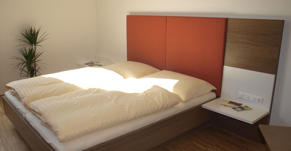 Moderní pokoj pro hosty s manželskou postelí, červeným čelem a rostlinami.