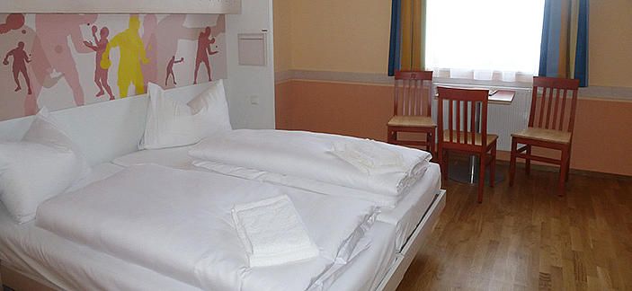 Hotelový pokoj s manželskou postelí, dvěma židlemi a stolem před oknem.