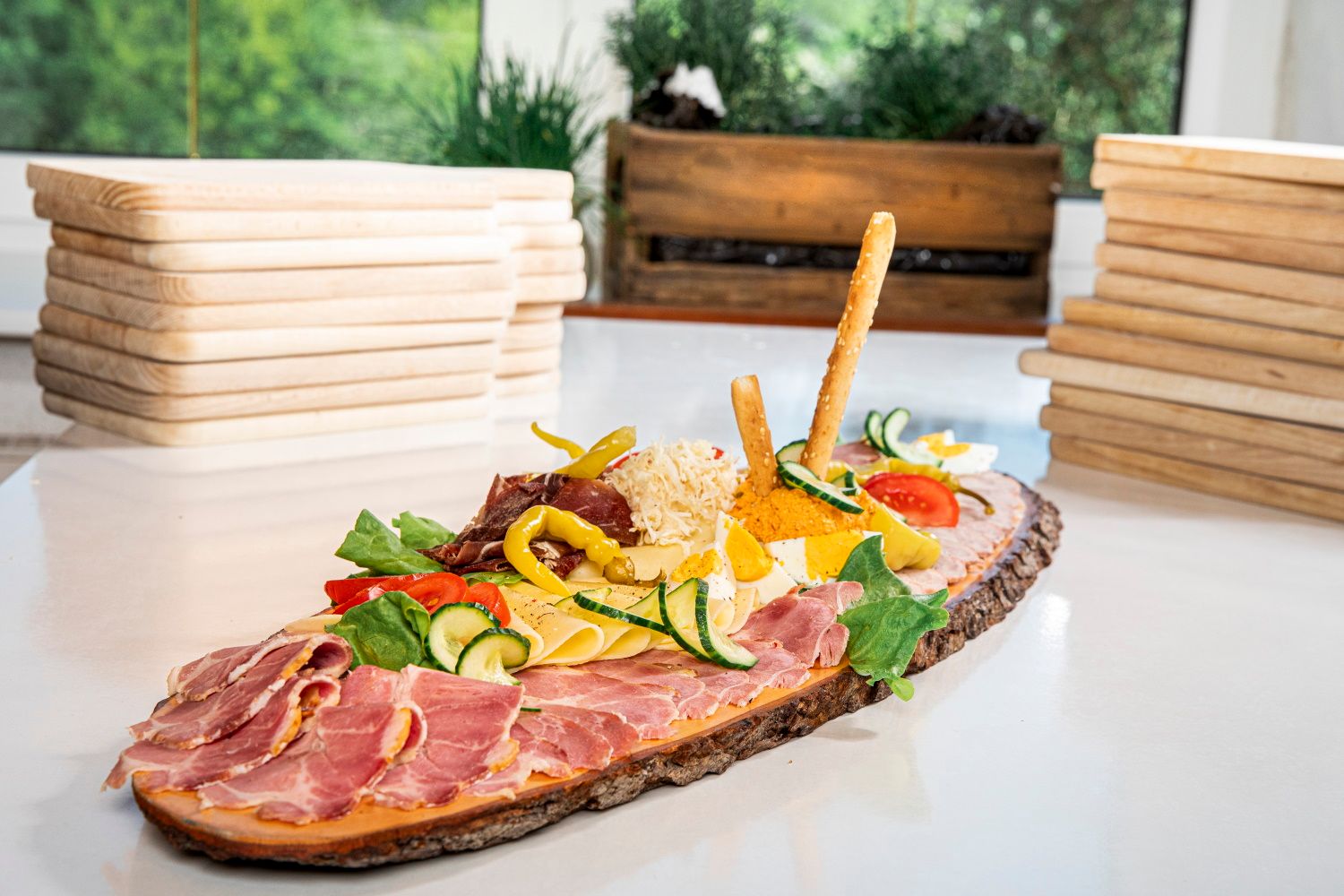 Talíř Heurigen se šunkou, sýrem, zeleninou a chlebovými tyčinkami na rustikálním dřevěném prkénku.