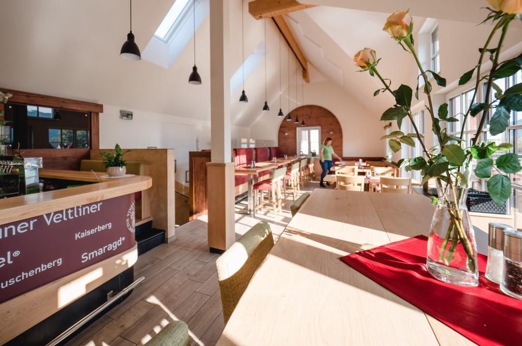 Pohled do interiéru moderního heurigera s dřevěným nábytkem a velkými okny.