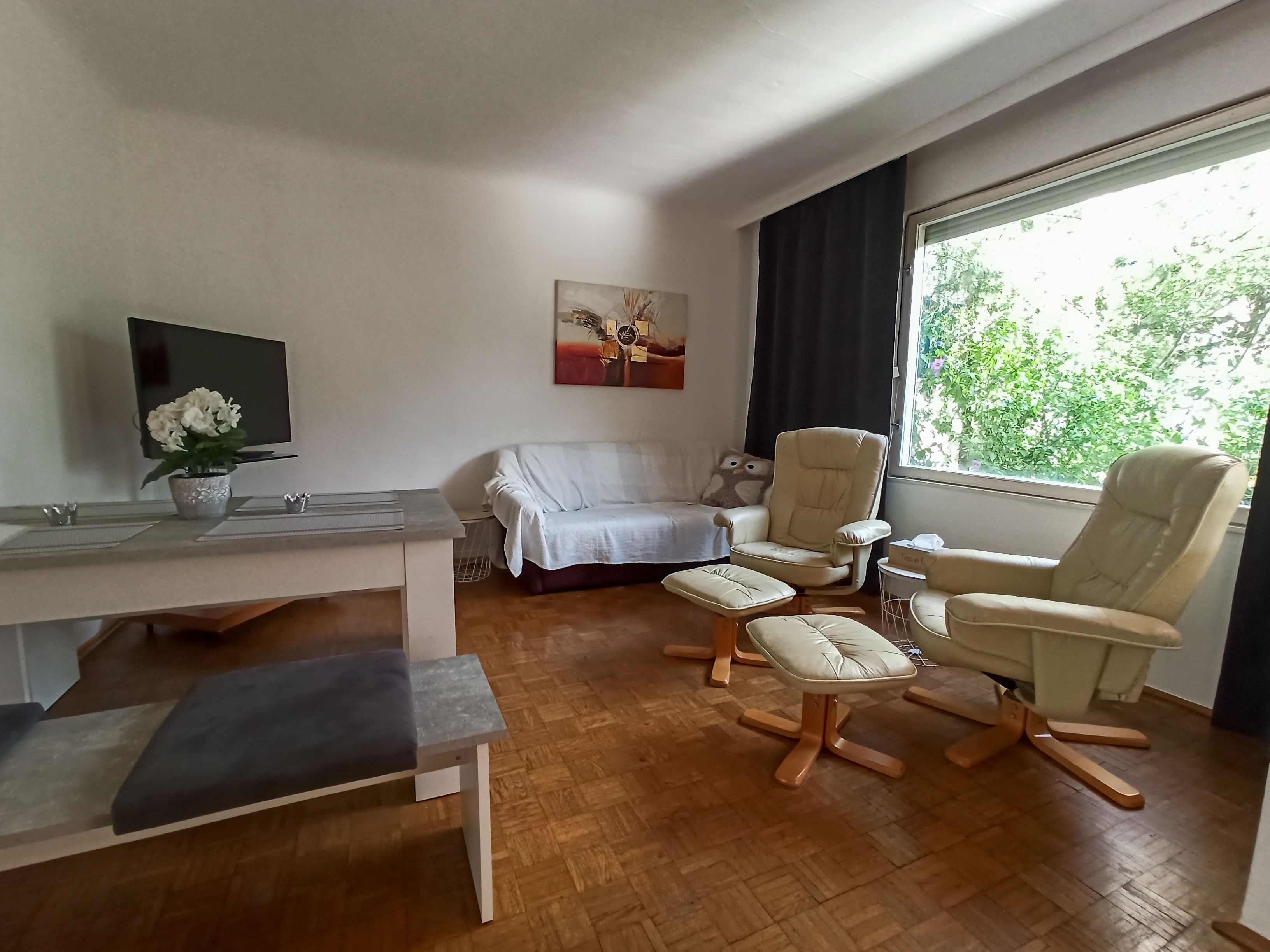 Obývací pokoj s pohovkou, dvěma křesly, stolem a velkým oknem.