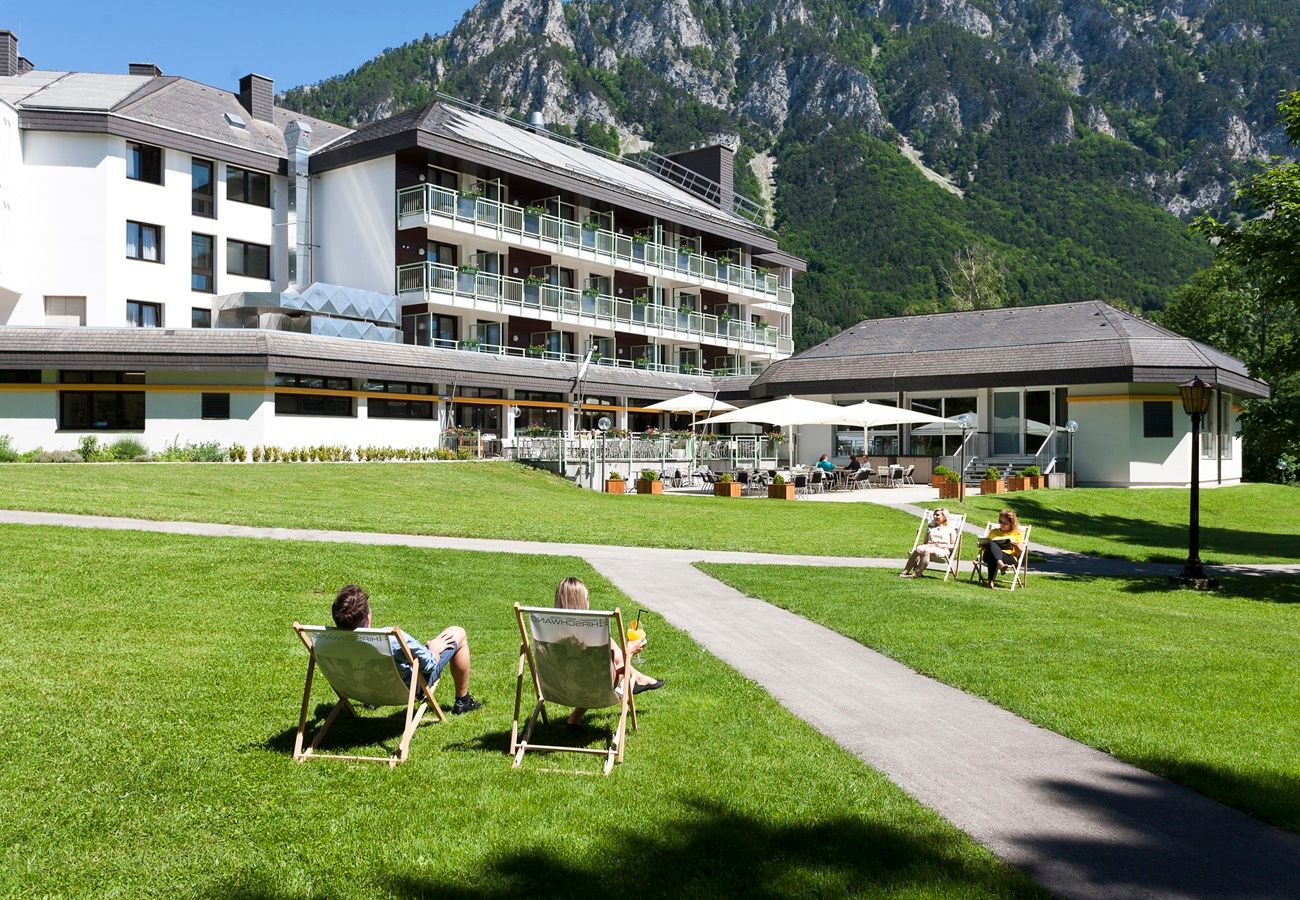 Hotel s terasou a lehátky na louce obklopené horami.