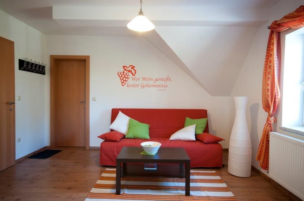 Útulný pokoj pro hosty s červenou pohovkou, polštáři, lampou a nástěnným citátem.