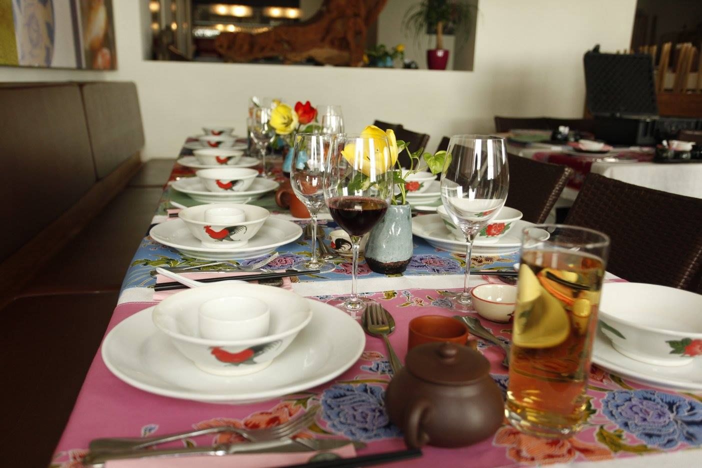 Stůl prostřený v restauraci s nádobím, sklenicemi a květinami.